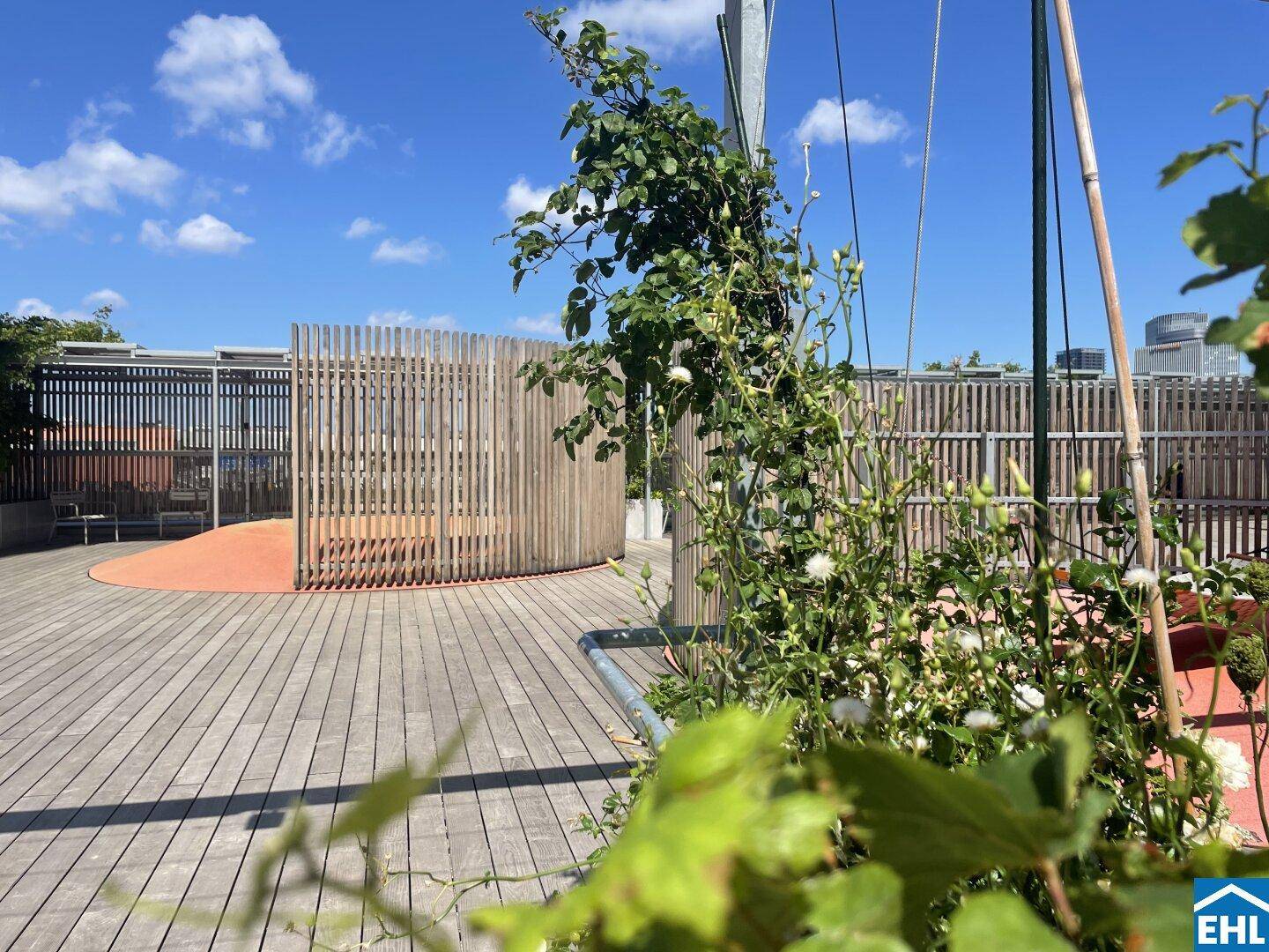 Dachterrasse mit Holzdeck, Pflanzen und dekorativen Holzabtrennungen für Gemeinschaftsbereiche.
