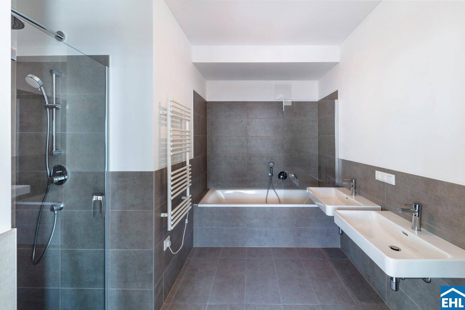 Modernes Badezimmer mit grauen Fliesen, Badewanne, begehbarer Dusche und Doppelwaschbecken.