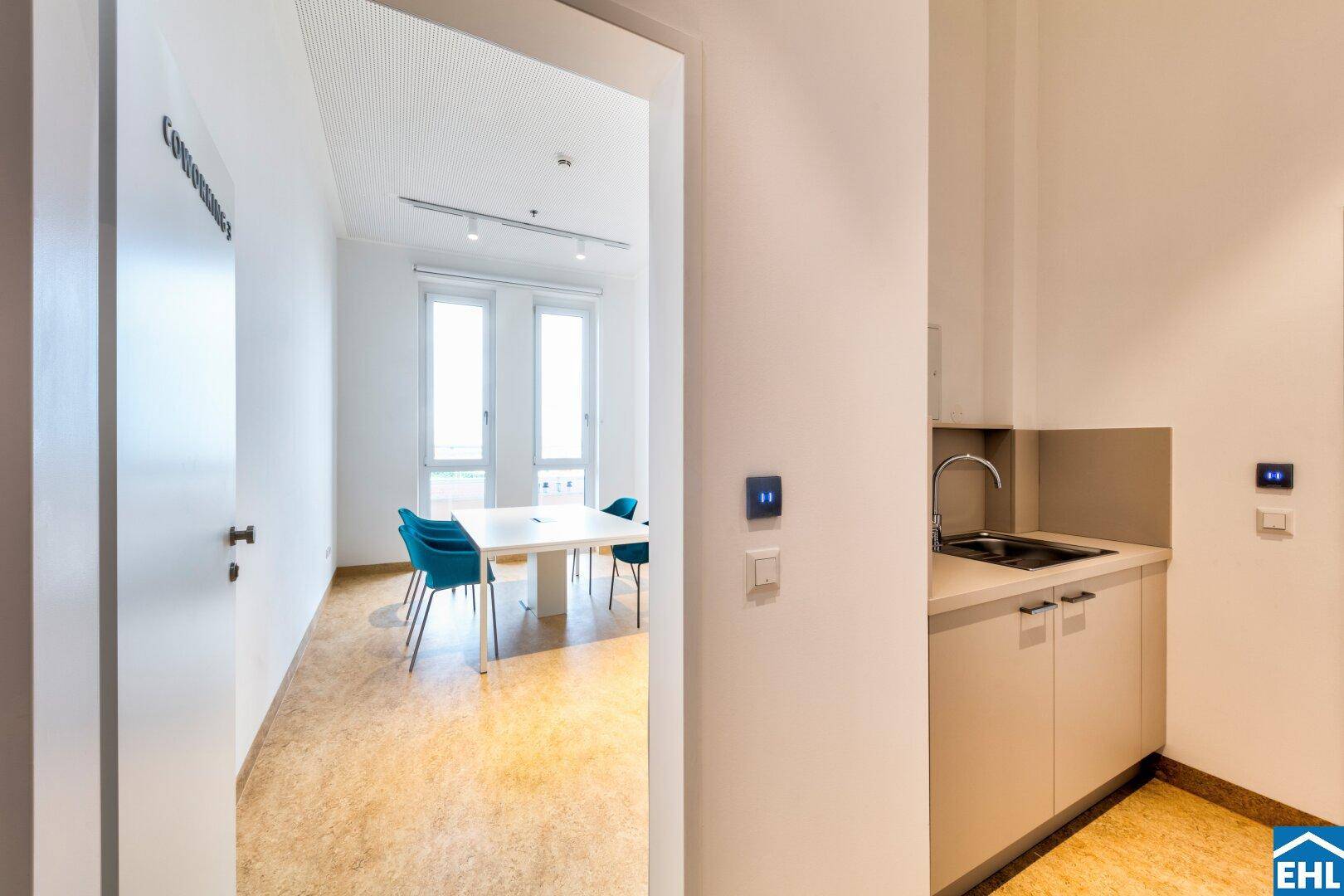 Kleiner Küchenbereich und angrenzender Coworking-Space mit modernen Möbeln und großen Fenstern.