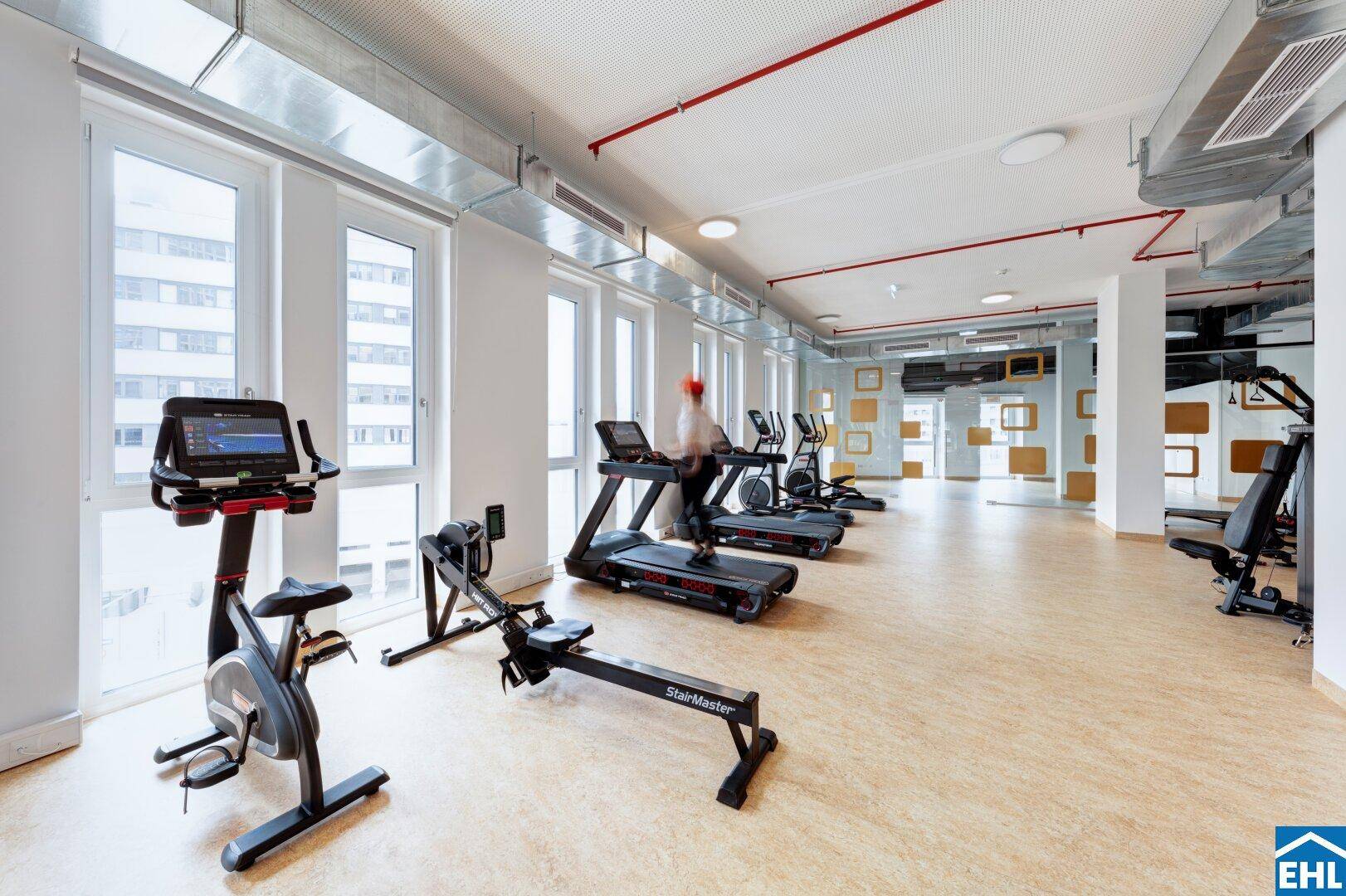 Heller Fitnessraum mit modernen Trainingsgeräten und großen Fenstern für viel Tageslicht.