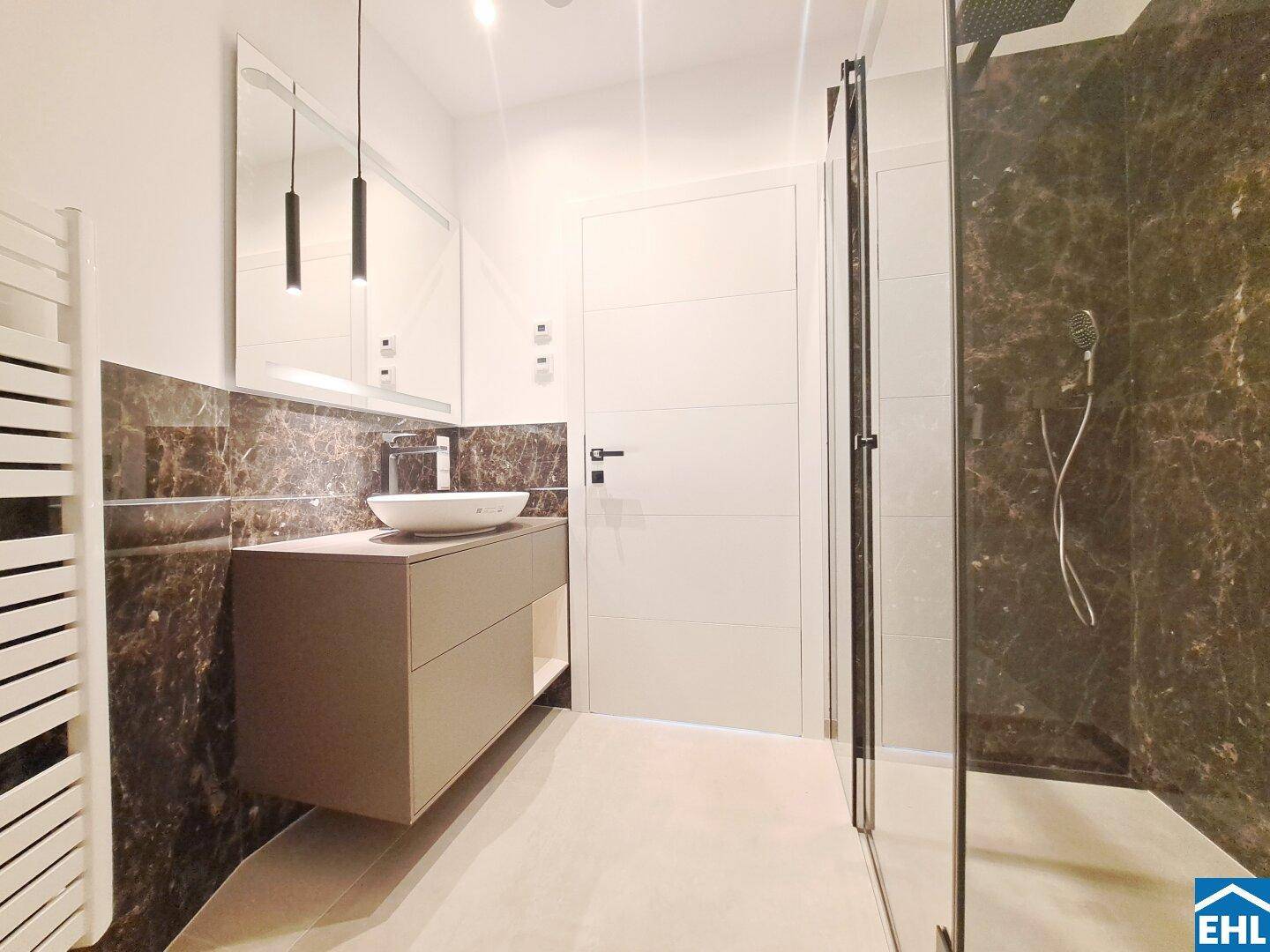 Stilvolles Badezimmer mit dunklen Marmorfliesen, modernem Waschtisch und begehbarer Dusche.