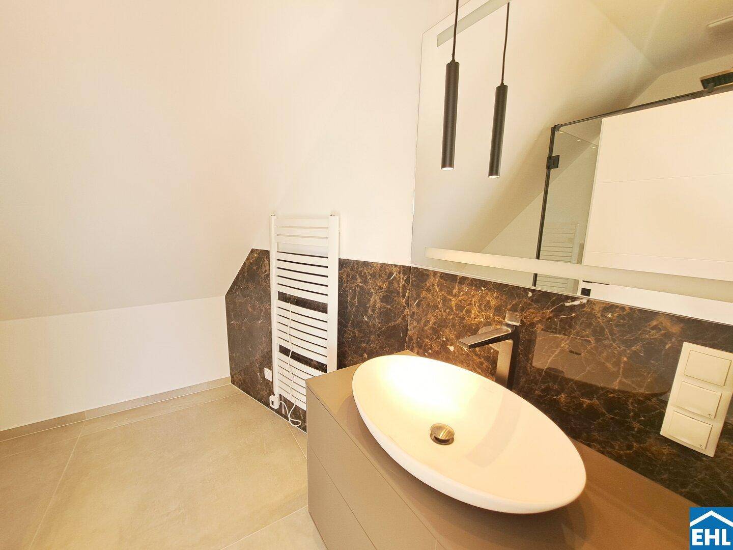 Modernes Badezimmer mit elegantem Waschbecken, dunklen Marmorfliesen und beheiztem Handtuchhalter.