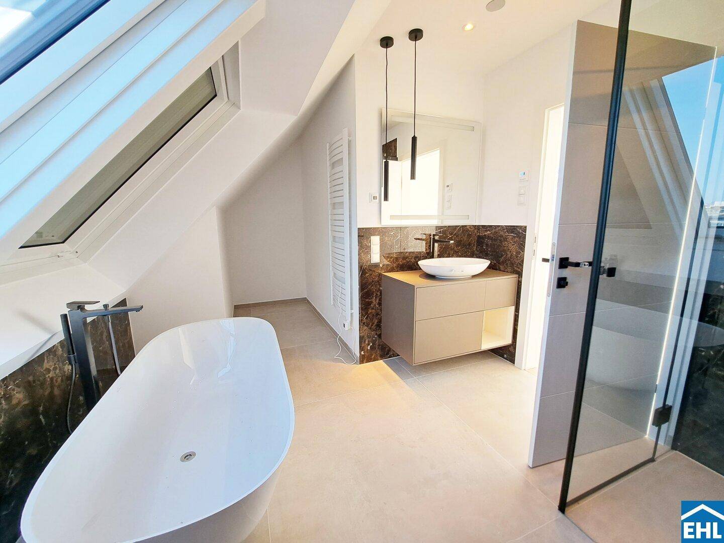 Luxuriöses Badezimmer mit freistehender Badewanne, Dachfenster und dunklen Marmoroberflächen.
