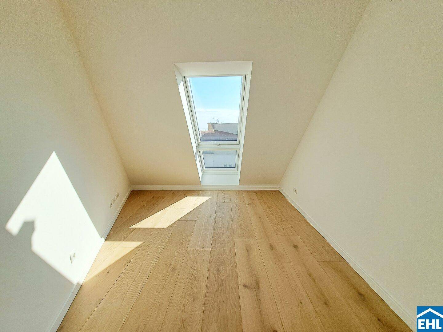 Gemütliches Dachzimmer mit Holzboden und einem einzelnen Dachfenster, das den Raum erhellt.