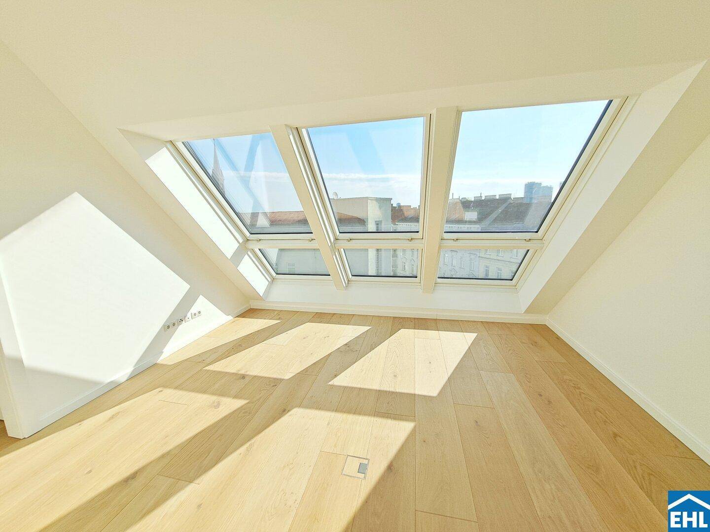 Heller Raum im Dachgeschoss mit schrägen Wänden und großen Dachfenstern für viel Tageslicht.