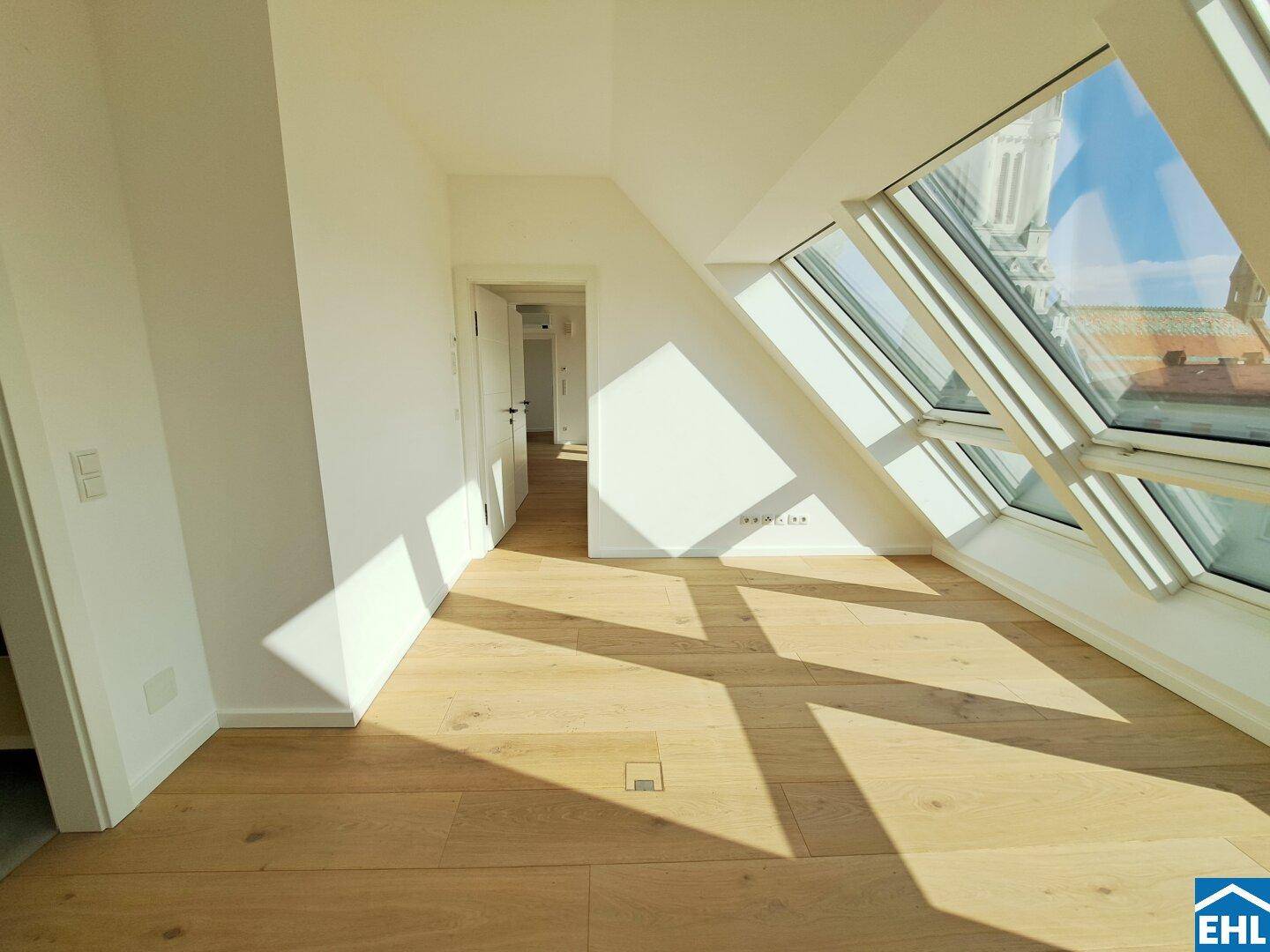 Dachgeschosszimmer mit Holzboden, schrägen Wänden und großen Fenstern, die den Raum erhellen.
