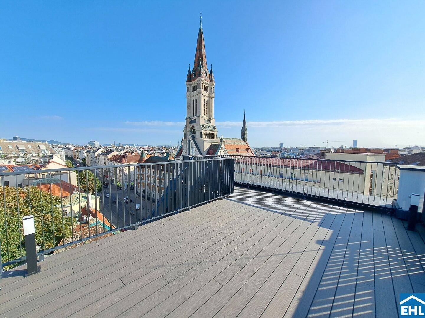 Geräumige Dachterrasse mit Holzboden und weitem Blick über die Stadt und eine Kirche.