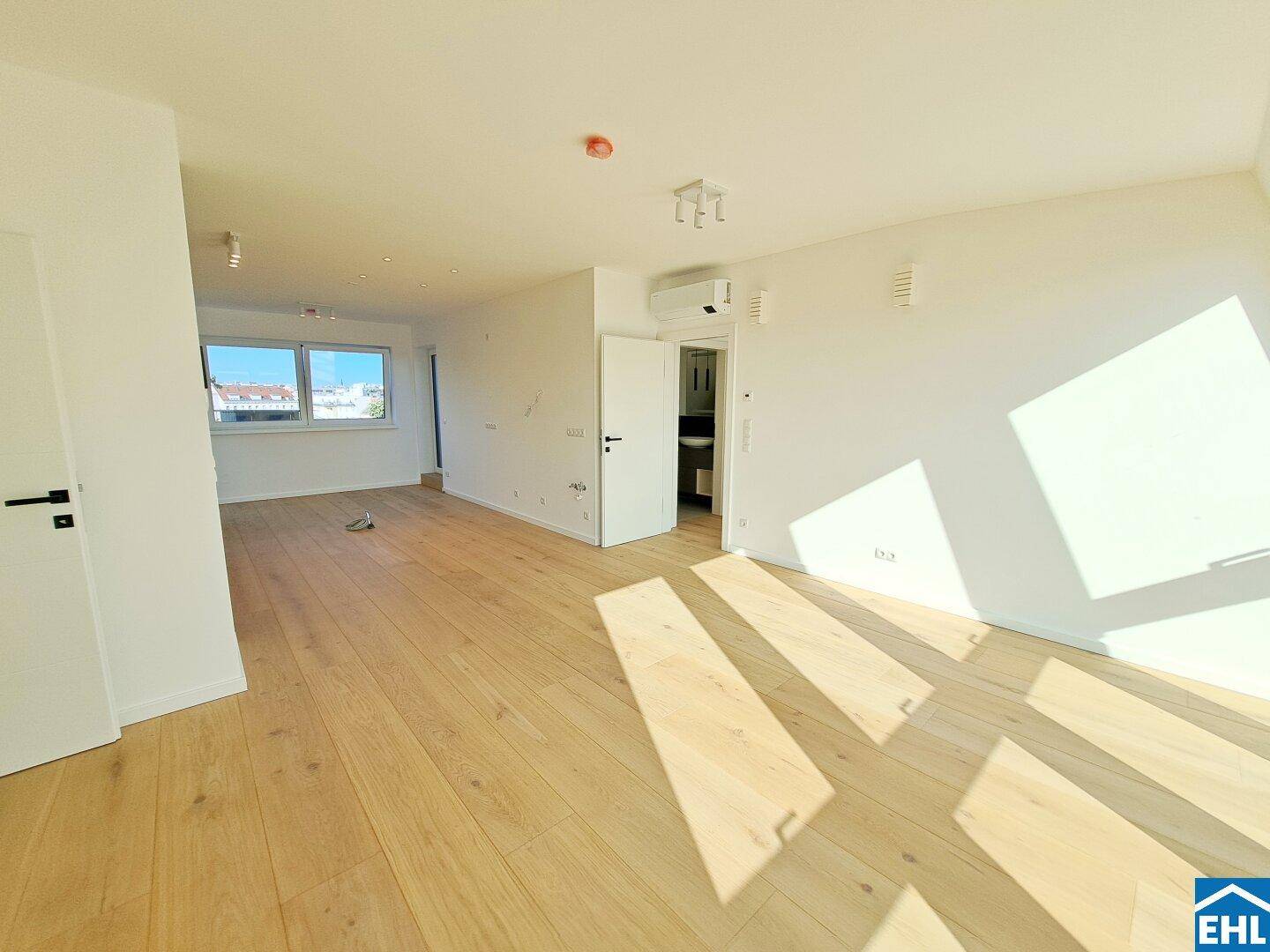 Lichtdurchfluteter Wohnbereich mit Holzboden und Zugang zu einem angrenzenden Badezimmer.