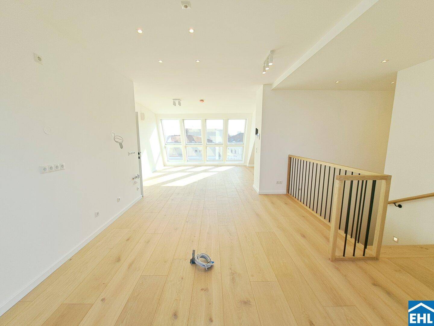 Geräumiger Wohnbereich mit Holztreppe und großen Dachfenstern, die viel Licht hereinlassen.