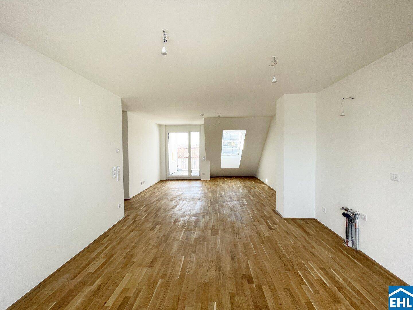 Geräumiger Wohnbereich mit Holzboden, Dachschrägen und Zugang zu einem Balkon.