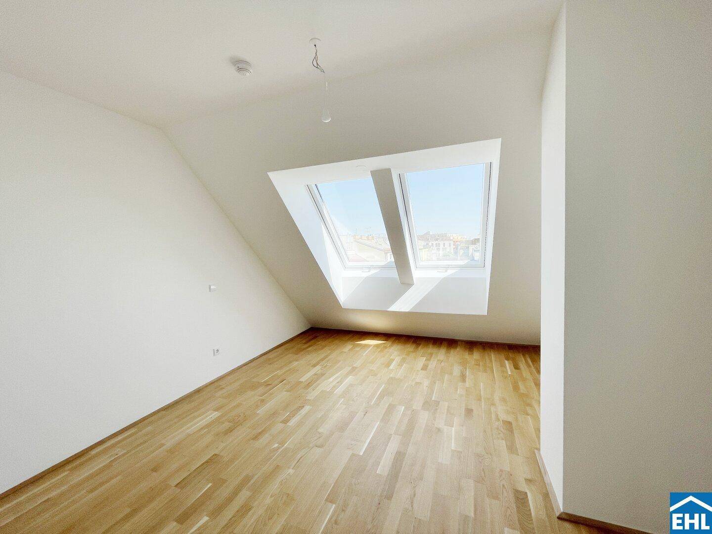 Geräumiges Zimmer im Dachgeschoss mit Holzboden und zwei großen Dachfenstern für viel Tageslicht.