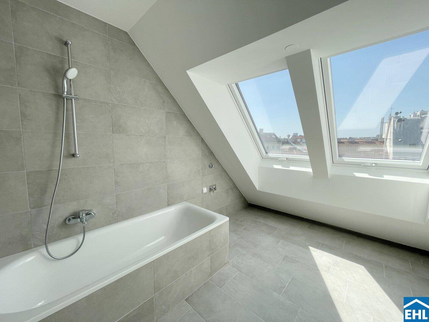 Modernes Badezimmer mit Badewanne, grauen Fliesen und großen Dachfenstern für viel Licht.