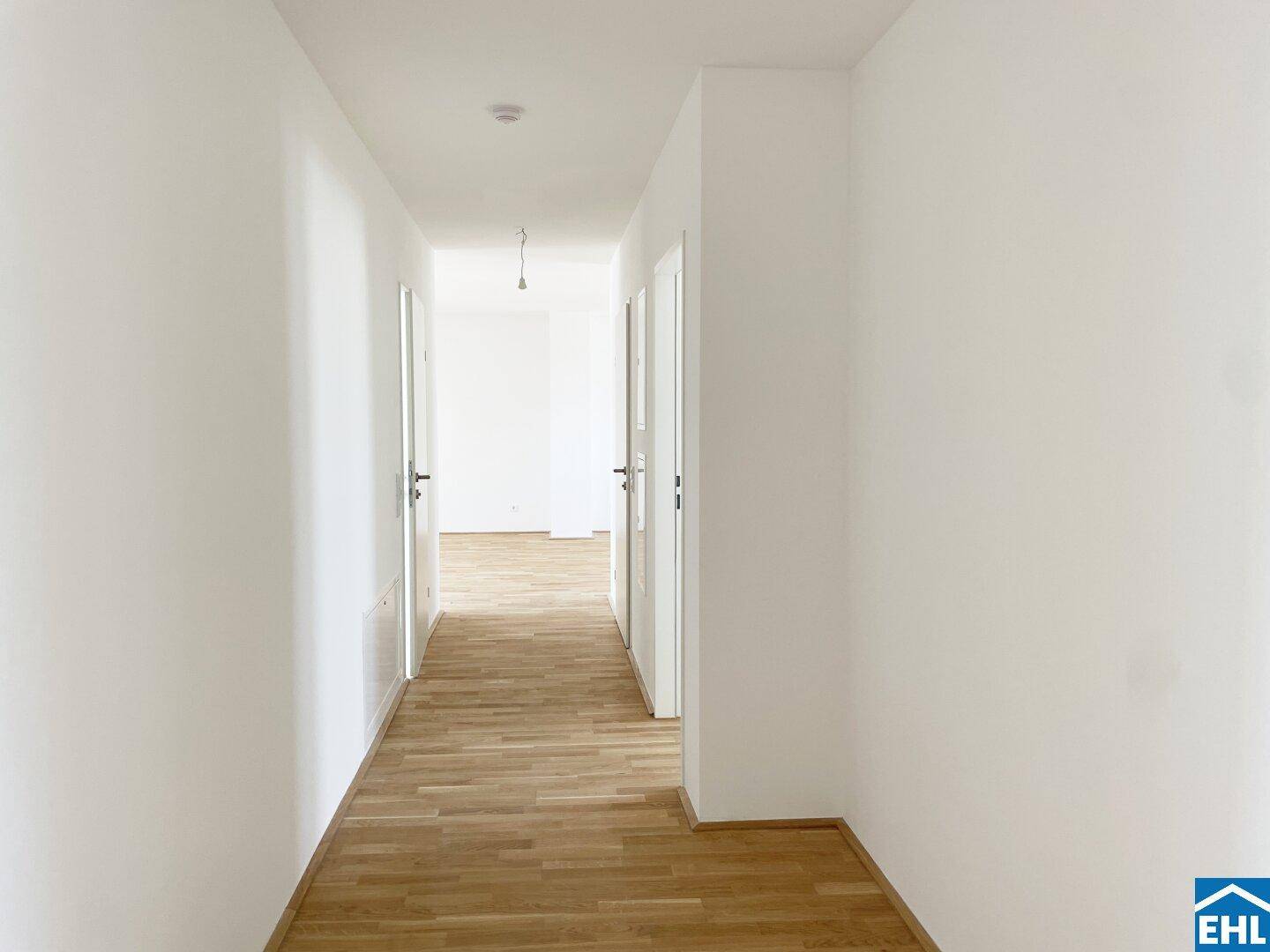 Heller Flur mit Holzboden und weißen Wänden, der zu den verschiedenen Zimmern führt.