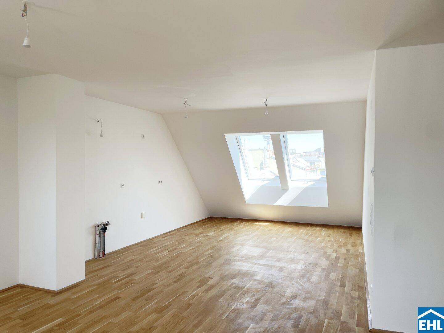 Lichtdurchfluteter Raum mit Holzboden und schrägen Wänden, ideal für ein gemütliches Wohnzimmer.