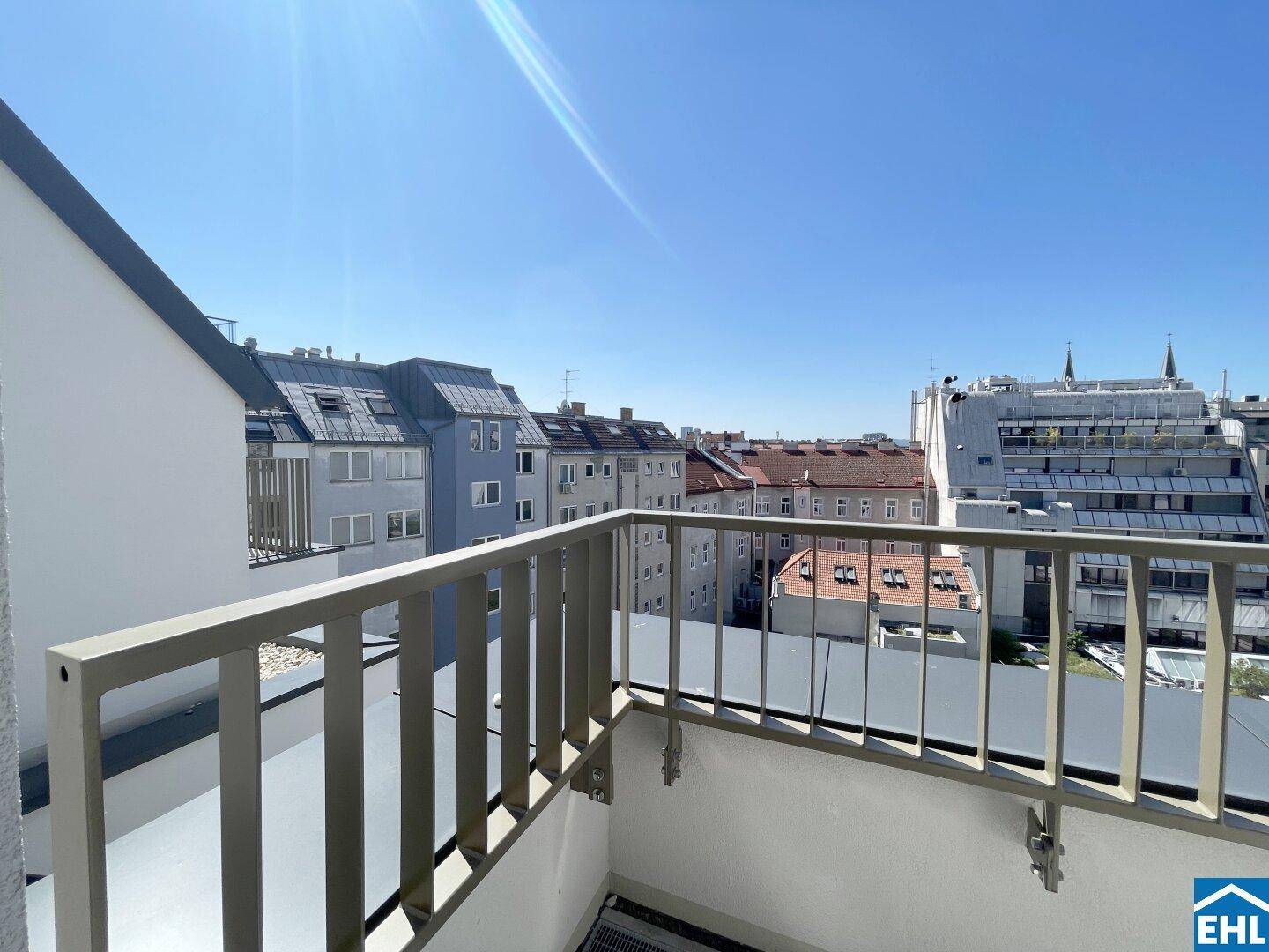 Sonniger Balkon mit Blick auf die Stadt und die umliegenden Wohngebäude unter blauem Himmel.