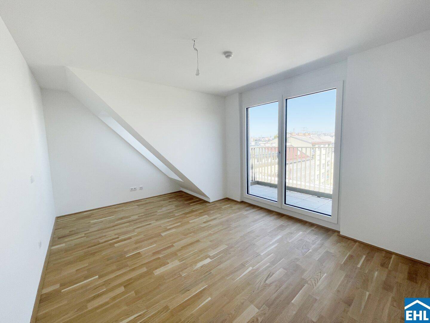 Helles Zimmer mit Holzboden, weiß gestrichenen Wänden und Zugang zu einem Balkon.