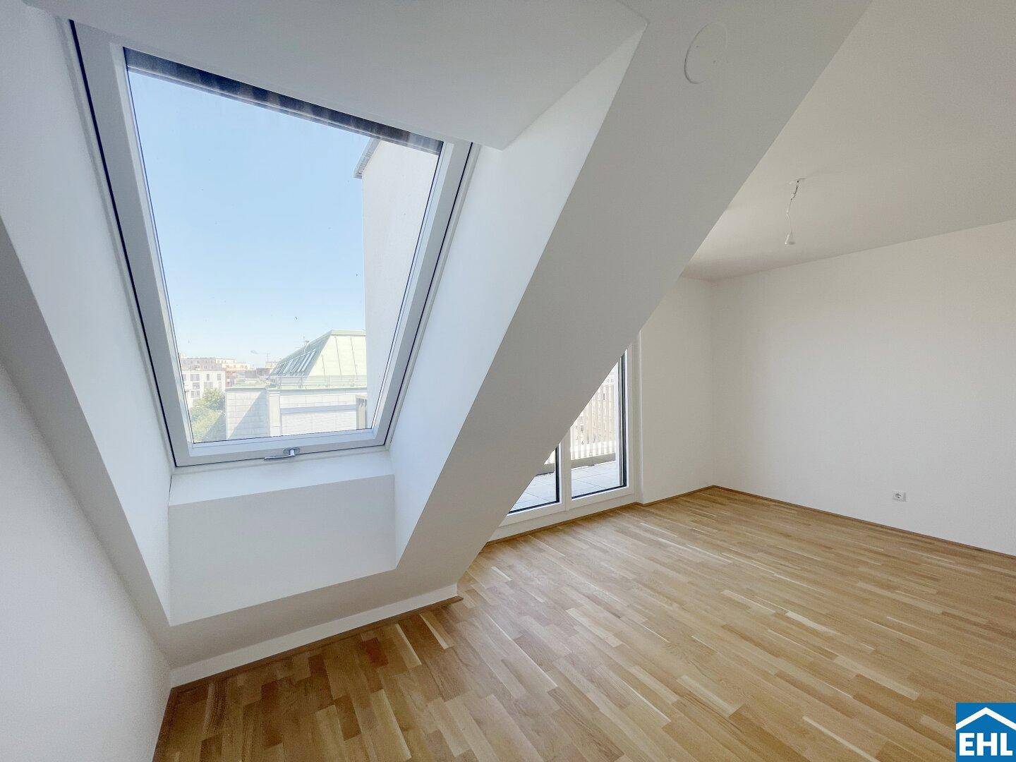 Dachzimmer mit Holzboden, weiß gestrichenen Wänden und einem großen Dachfenster.
