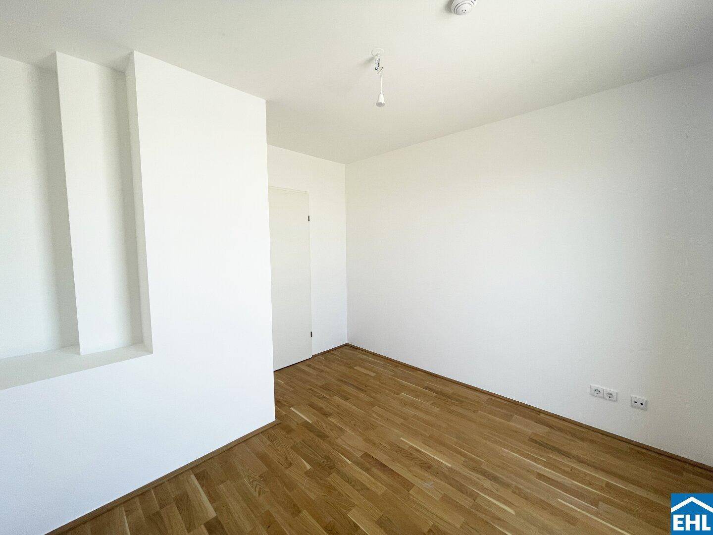Leerer Raum mit Holzboden, weißen Wänden und einer dekorativen Nische.