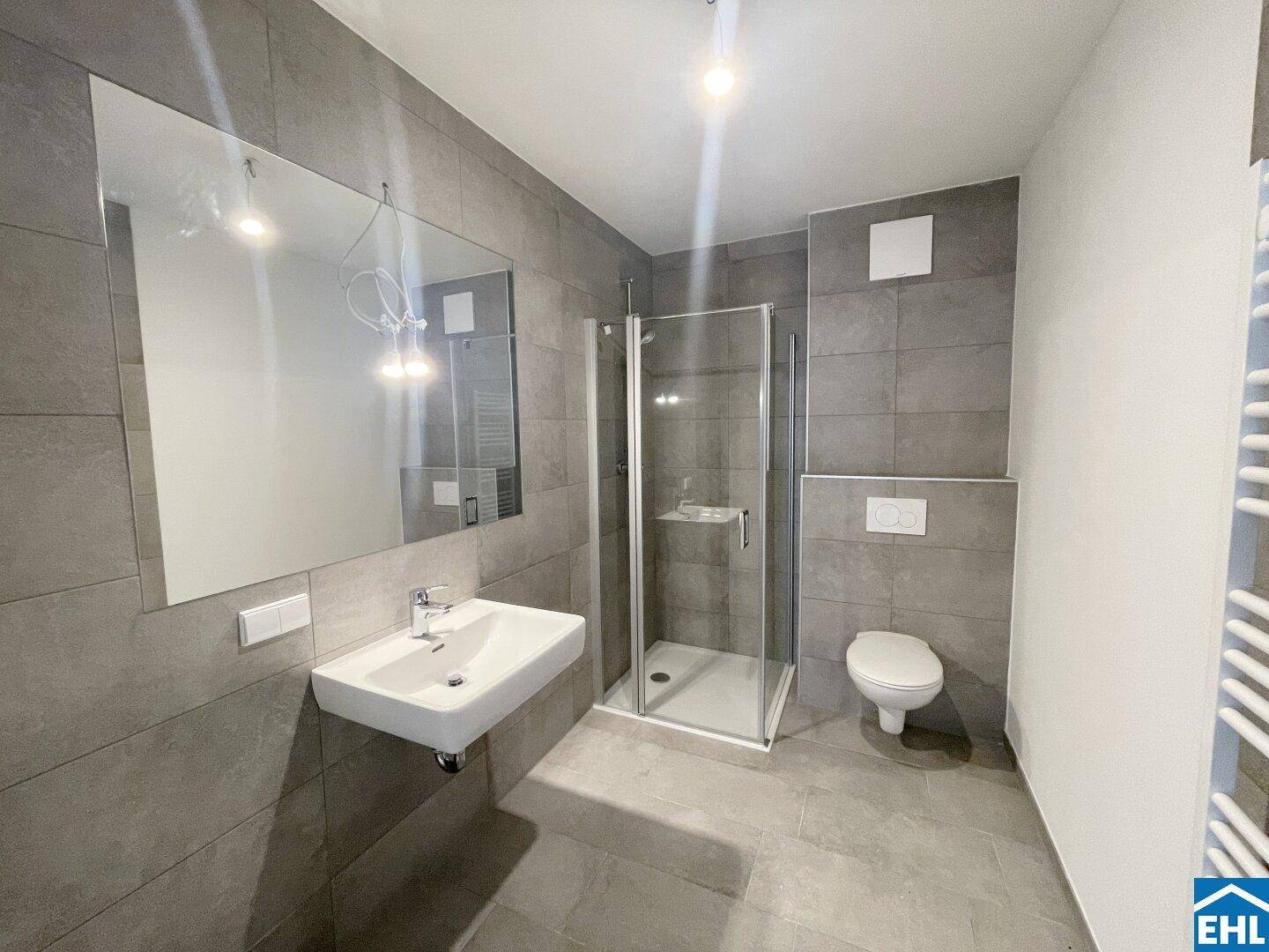 Modernes Badezimmer mit grauen Fliesen, Duschkabine und wandhängendem WC.