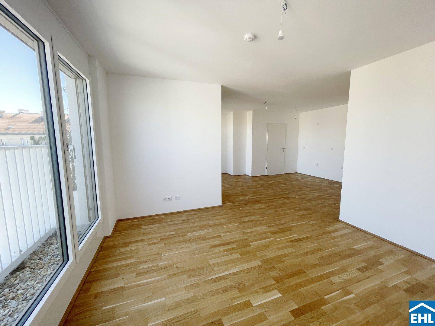 Heller, leerer Raum mit Parkettboden und großen Fenstern, die Zugang zu einem Balkon bieten.