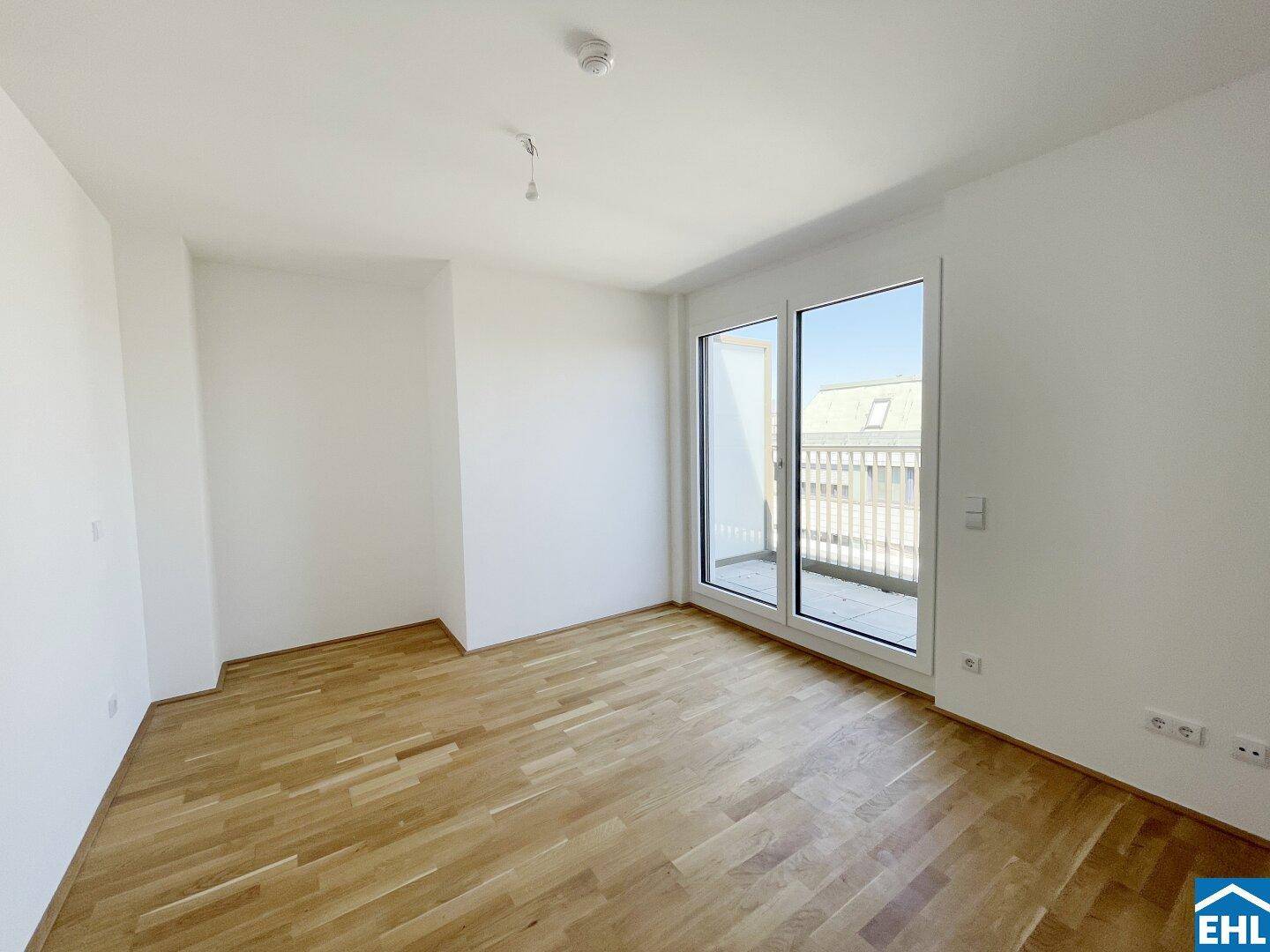 Lichtdurchfluteter Raum mit Parkettboden und Zugang zu einem Balkon, ideal für ein Schlafzimmer.