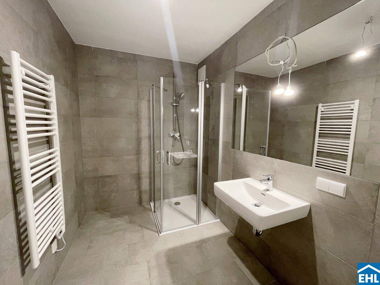 Modernes Badezimmer mit grauen Fliesen, ebenerdiger Dusche und beheiztem Handtuchhalter.