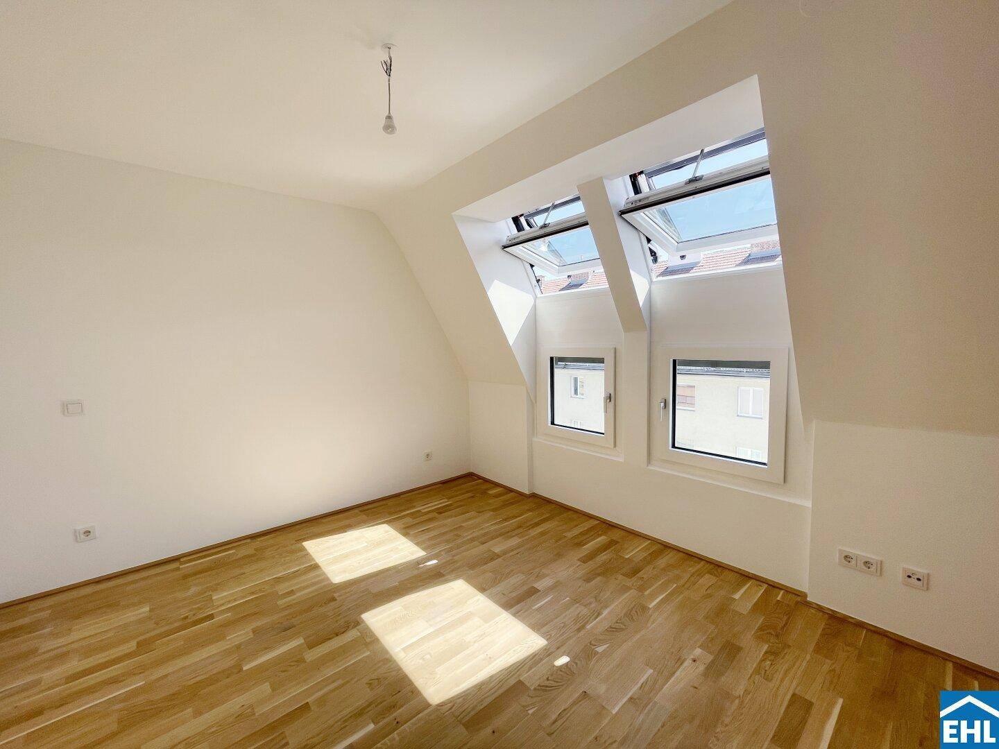 Helles Dachzimmer mit Holzboden, weißen Wänden und mehreren Dachfenstern für viel Licht.