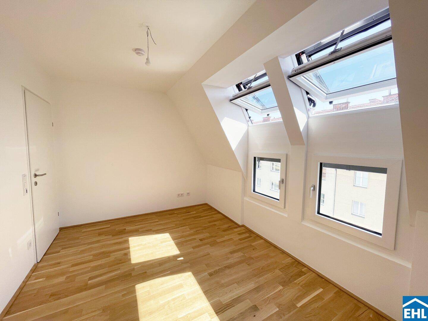 Geräumiges Dachzimmer mit Holzboden und schrägen Wänden, ausgestattet mit Dach- und Vertikalfenstern.
