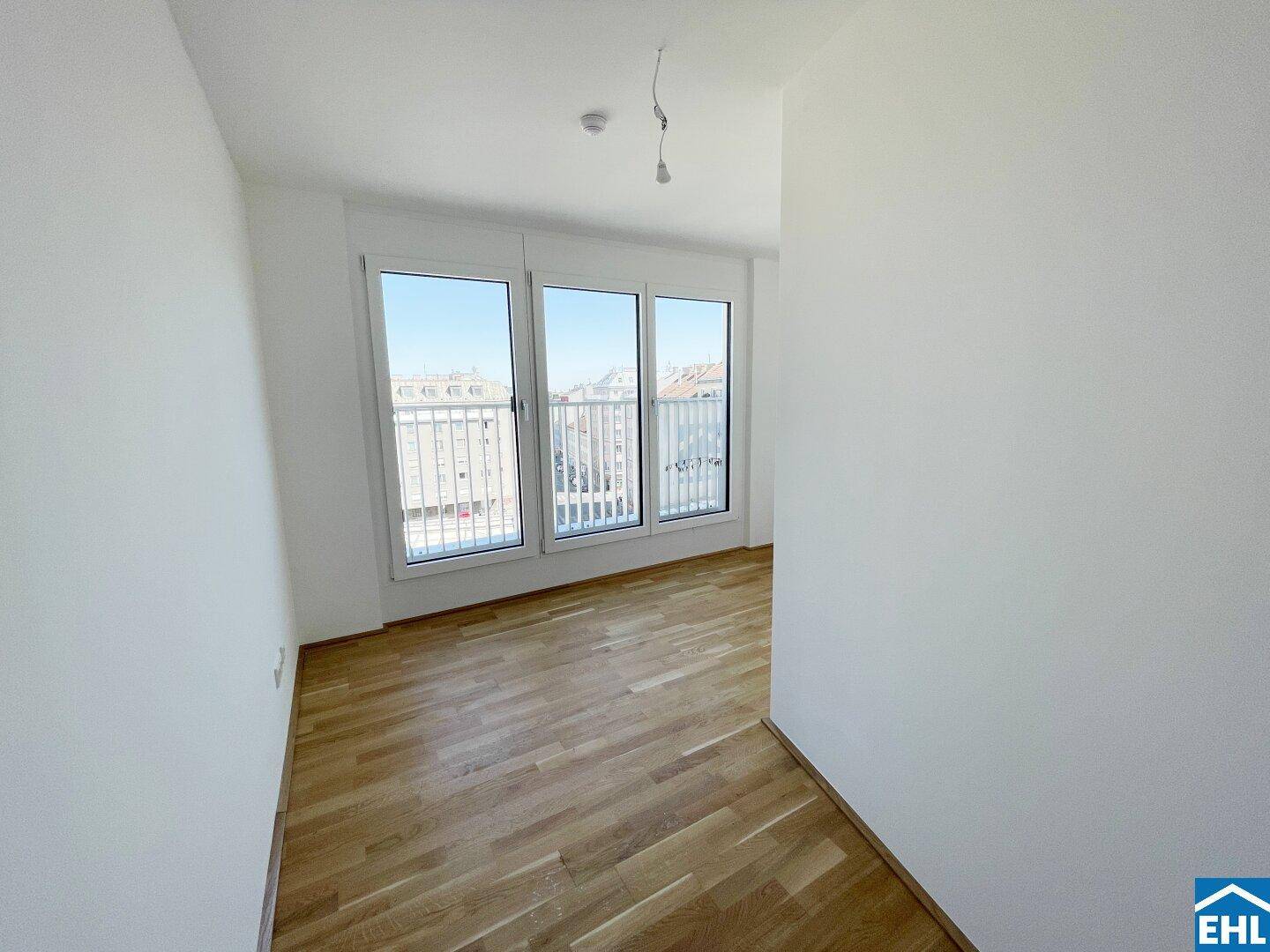 Lichtdurchflutetes Zimmer mit Holzboden und breiten Fenstern, die einen urbanen Ausblick ermöglichen.
