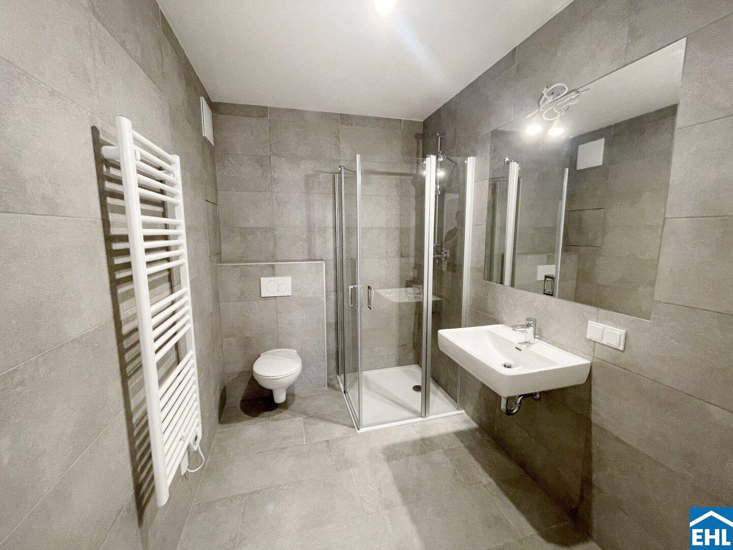 Modernes Badezimmer mit grauen Fliesen, ebenerdiger Dusche, Wand-WC und beheiztem Handtuchhalter.