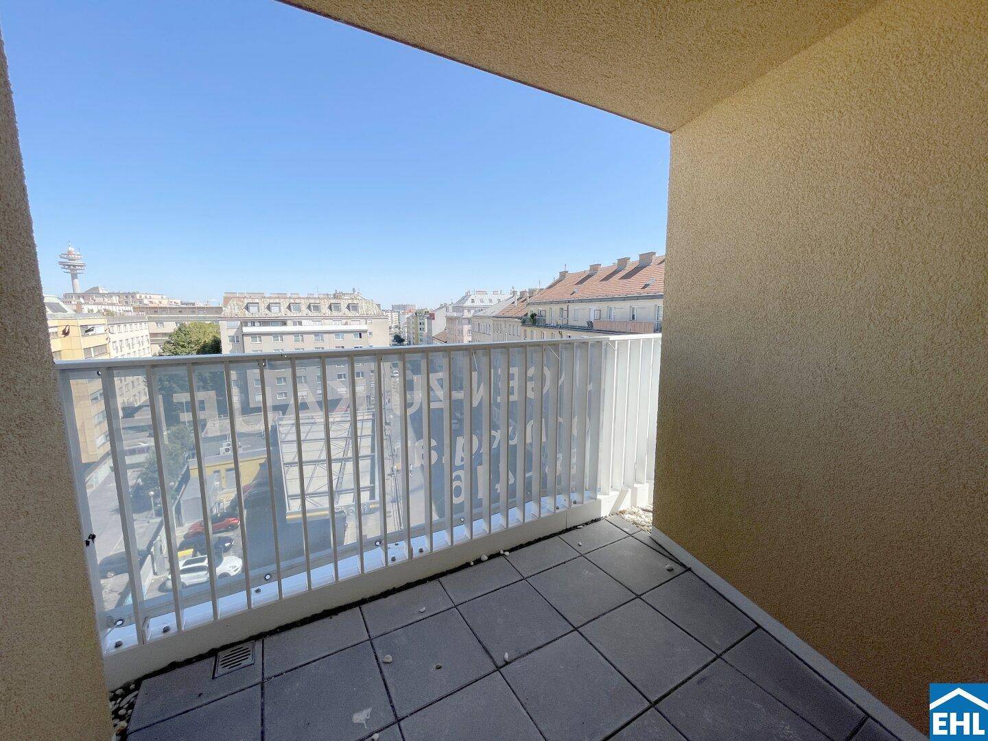 Heller Balkon mit Fliesenboden und Glasgeländer, der einen weiten Blick über die Stadt bietet.
