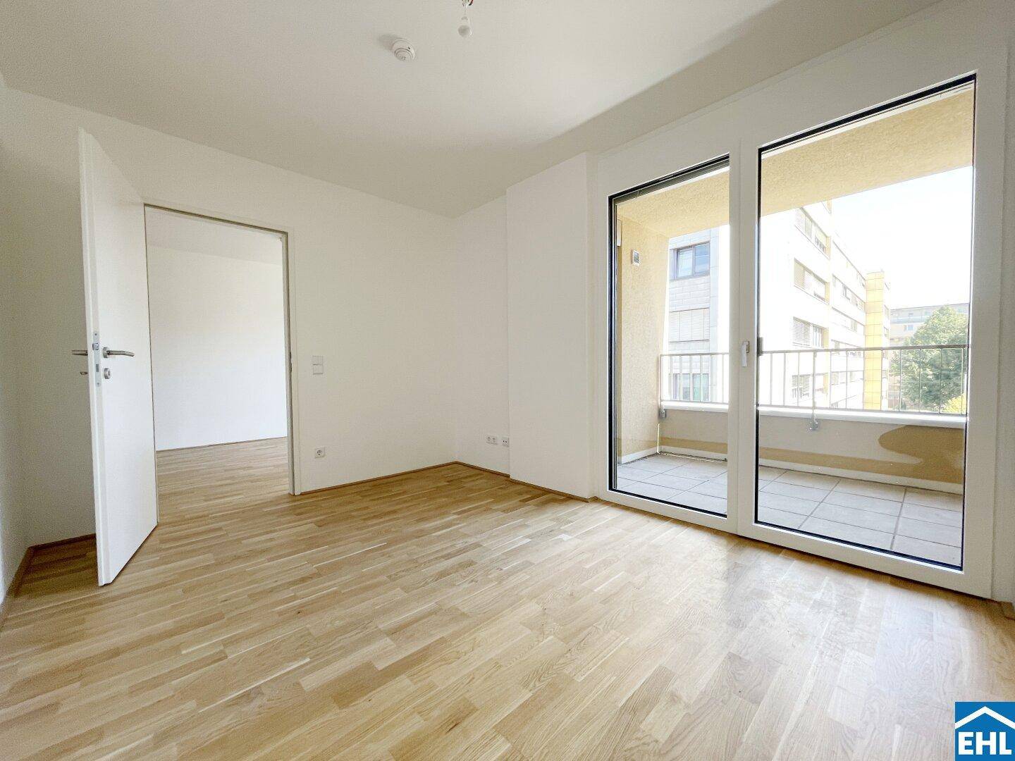 Heller Raum mit Parkettboden und großen Fenstern, die einen Zugang zum Balkon bieten.