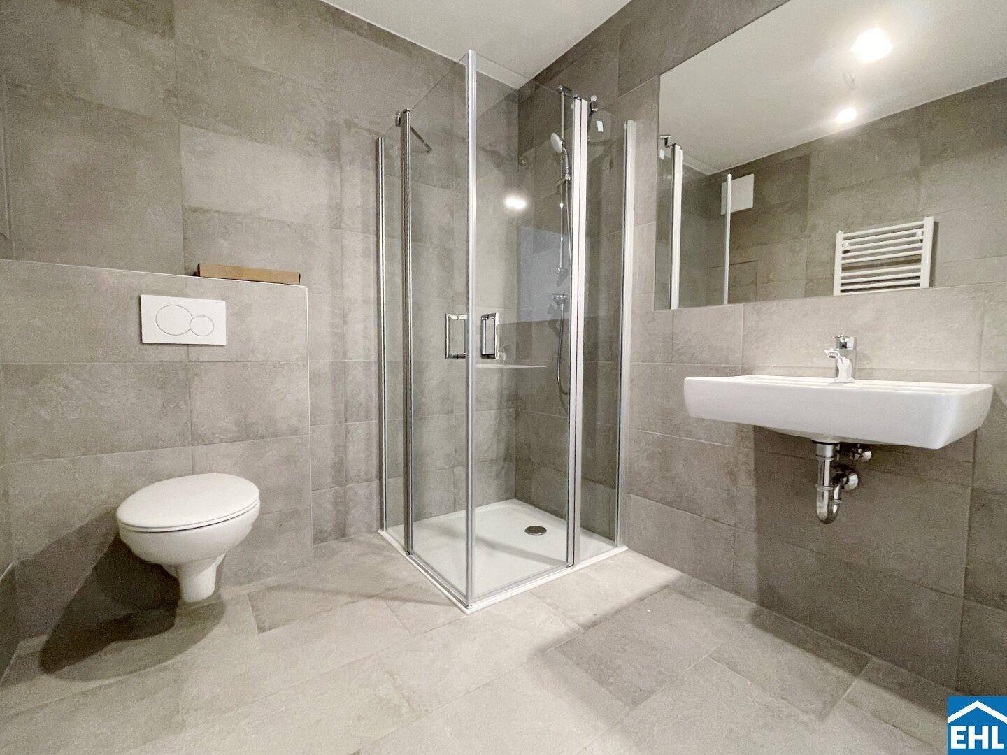 Modernes Badezimmer mit grauen Fliesen, einer Duschkabine, wandhängendem WC und einem eleganten Waschtisch.