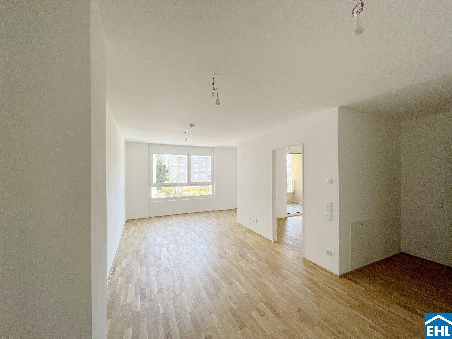Geräumiges, helles Zimmer mit Parkettboden und großen Fenstern, das viel Tageslicht hereinlässt.