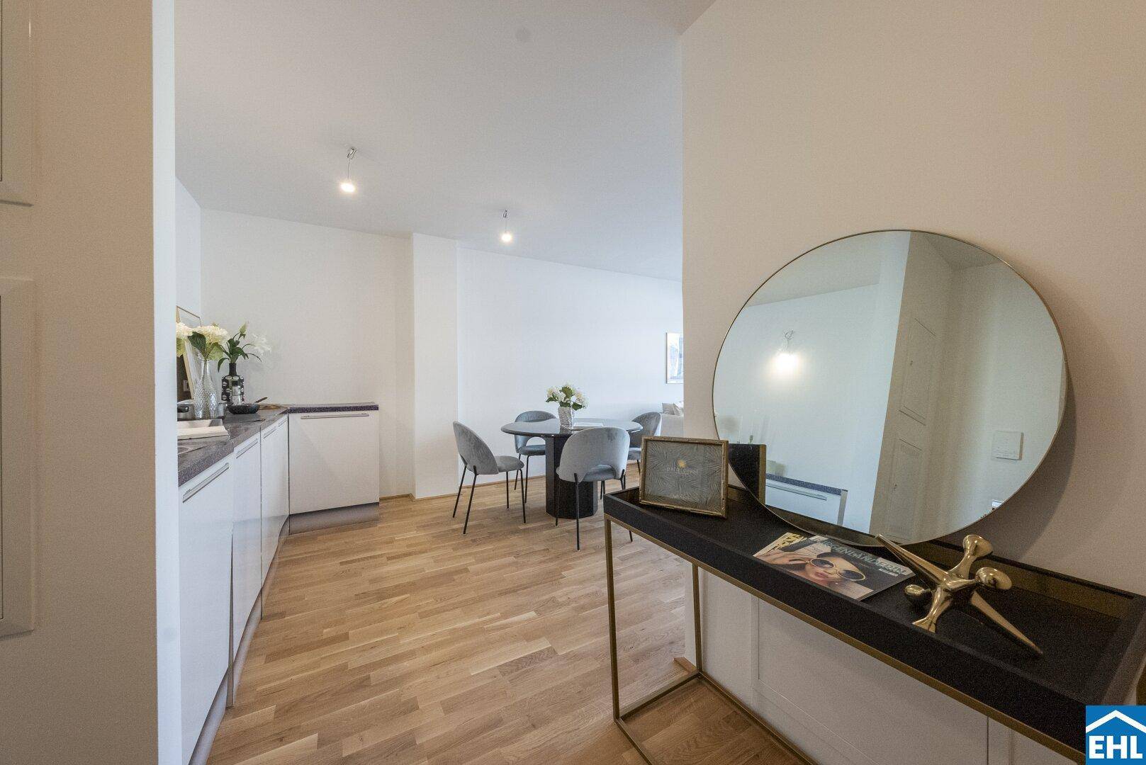 Offener Wohnbereich mit integrierter Küchenzeile, Esstisch und modernem Spiegel, ideal für geselliges Beisammensein.