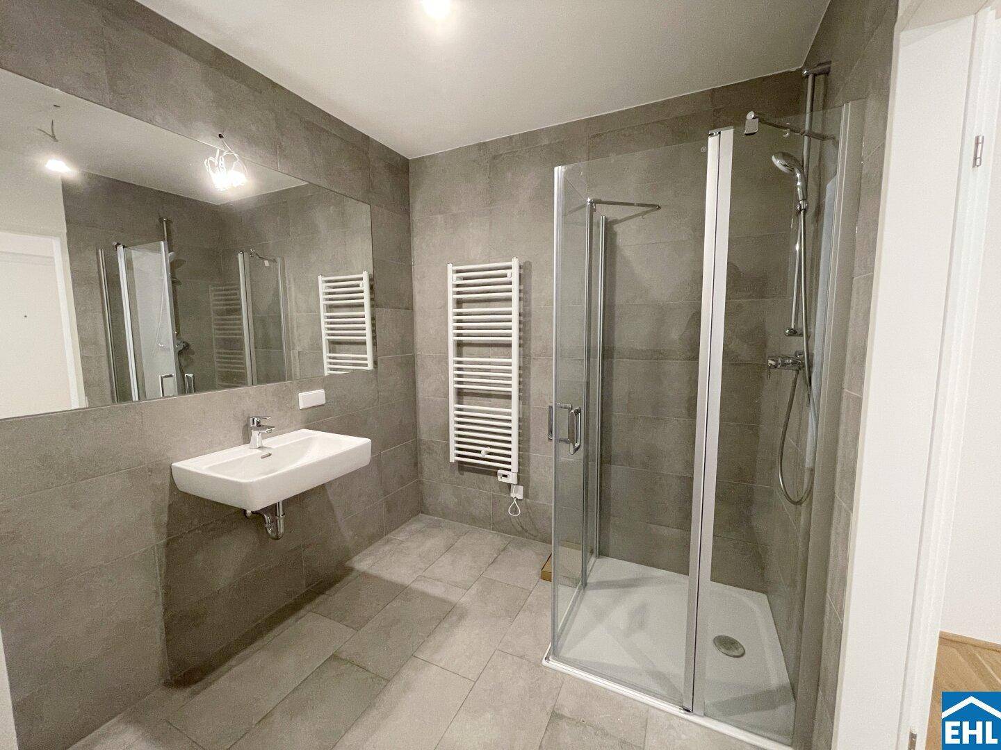 Modernes Badezimmer mit grauen Fliesen, Duschkabine, Einzelwaschbecken und Handtuchheizkörper.