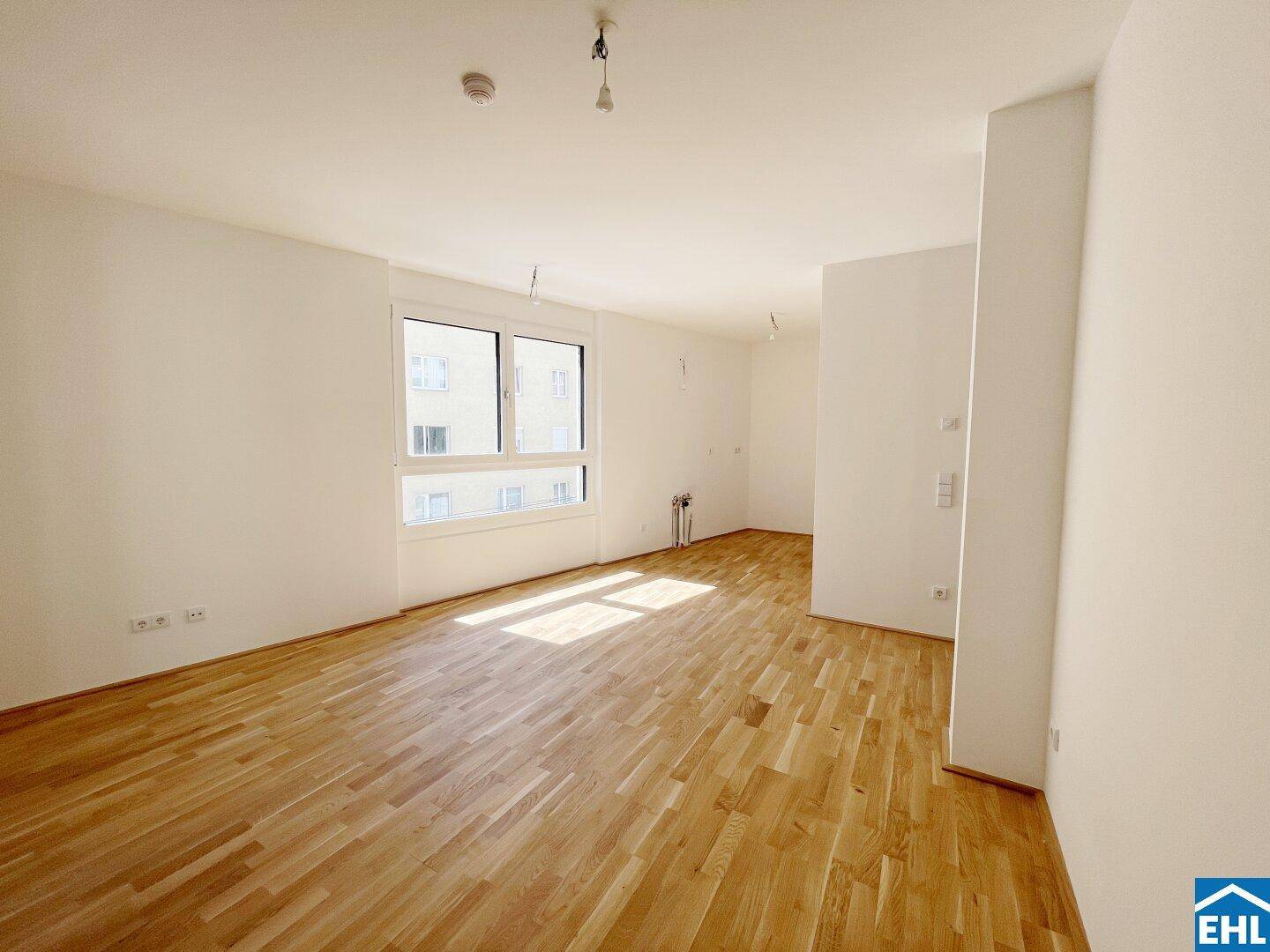 Helles, leeres Wohnzimmer mit Parkettboden und großen Fenstern, bereit zur individuellen Gestaltung.