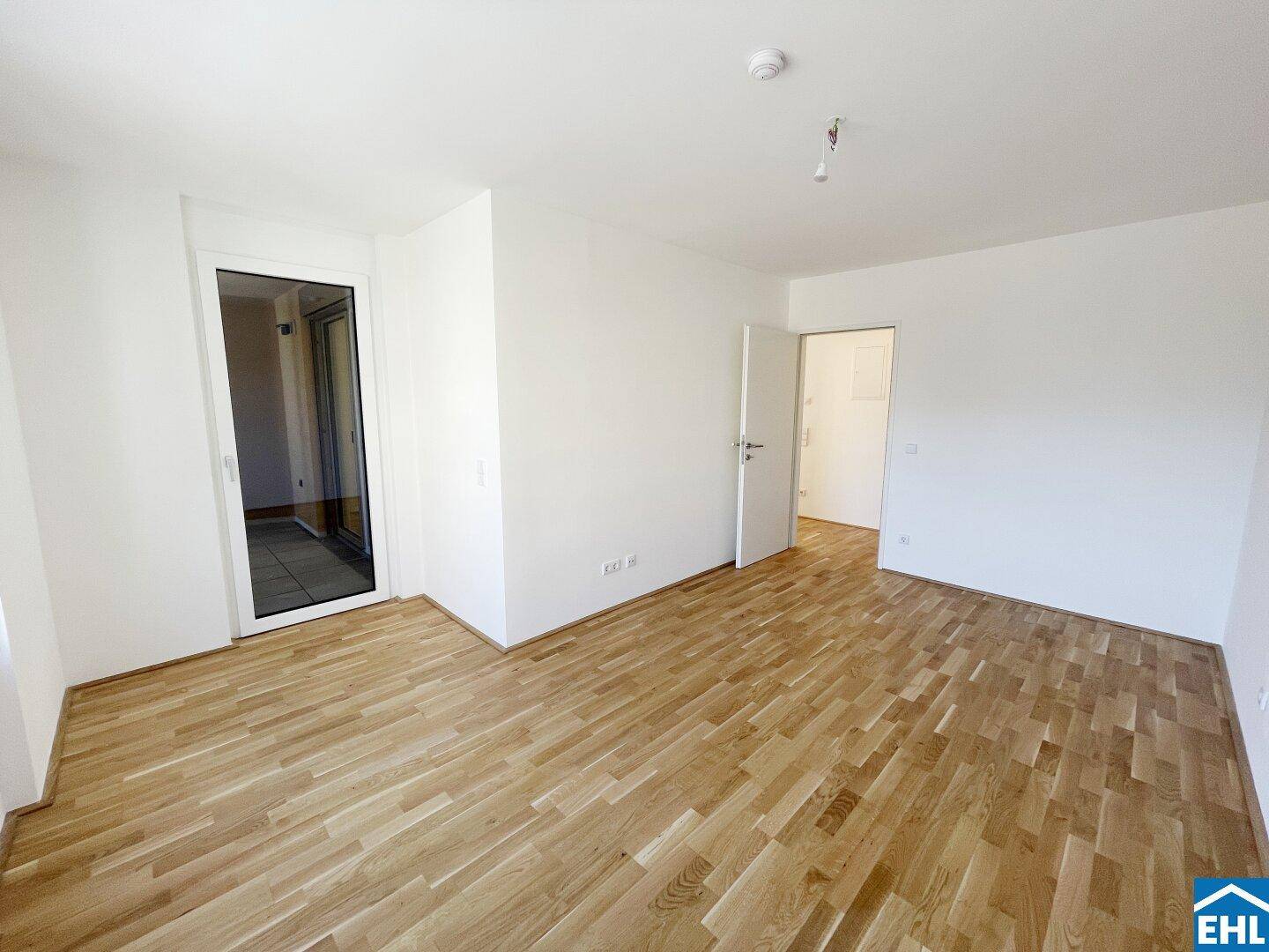 Geräumiges, unmöbliertes Zimmer mit Parkettboden und Zugang zu einem weiteren Raum sowie einem Balkon.