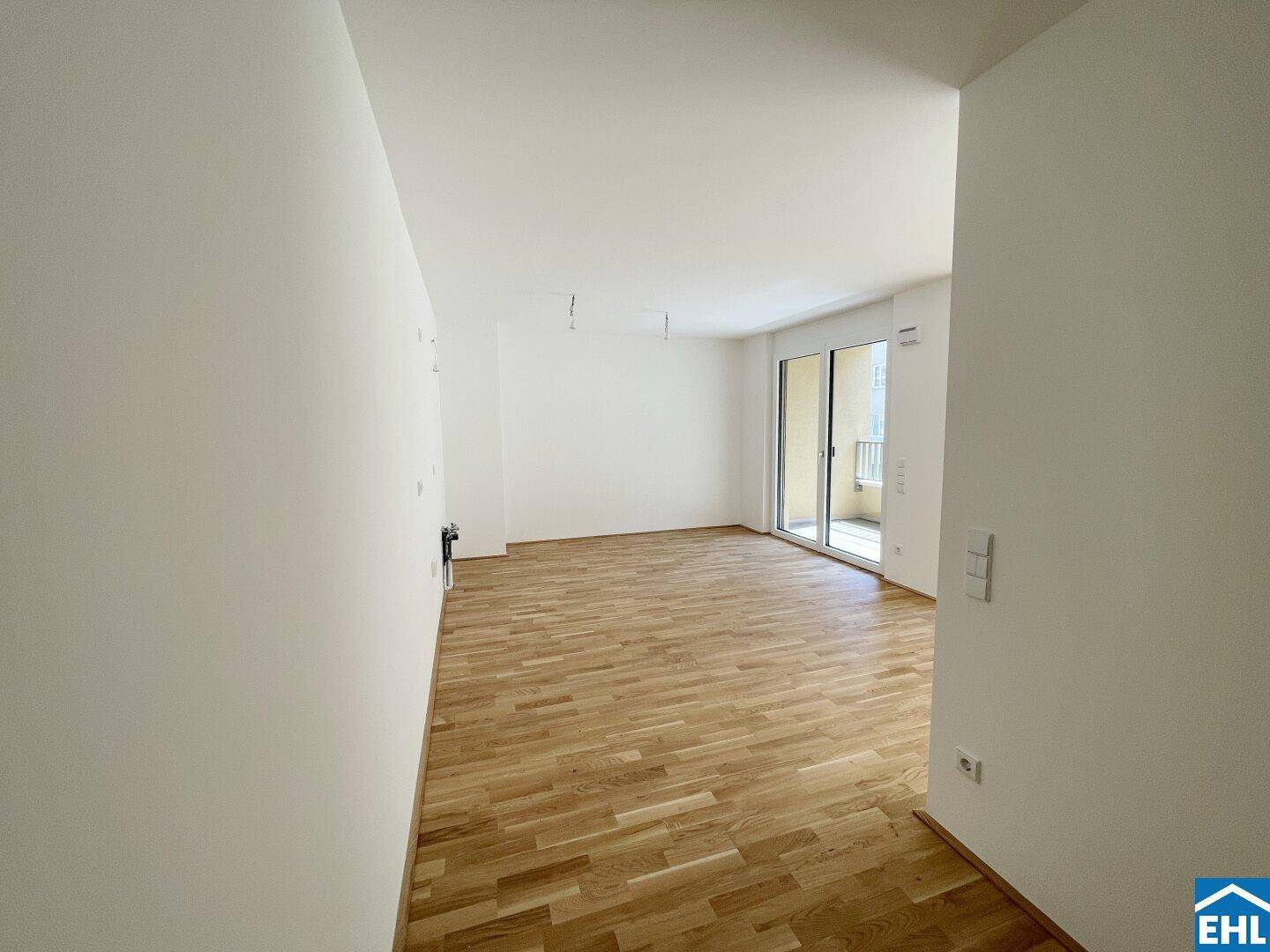 Heller Wohnbereich mit Parkettboden und großem Balkonzugang, der viel Tageslicht hereinlässt.