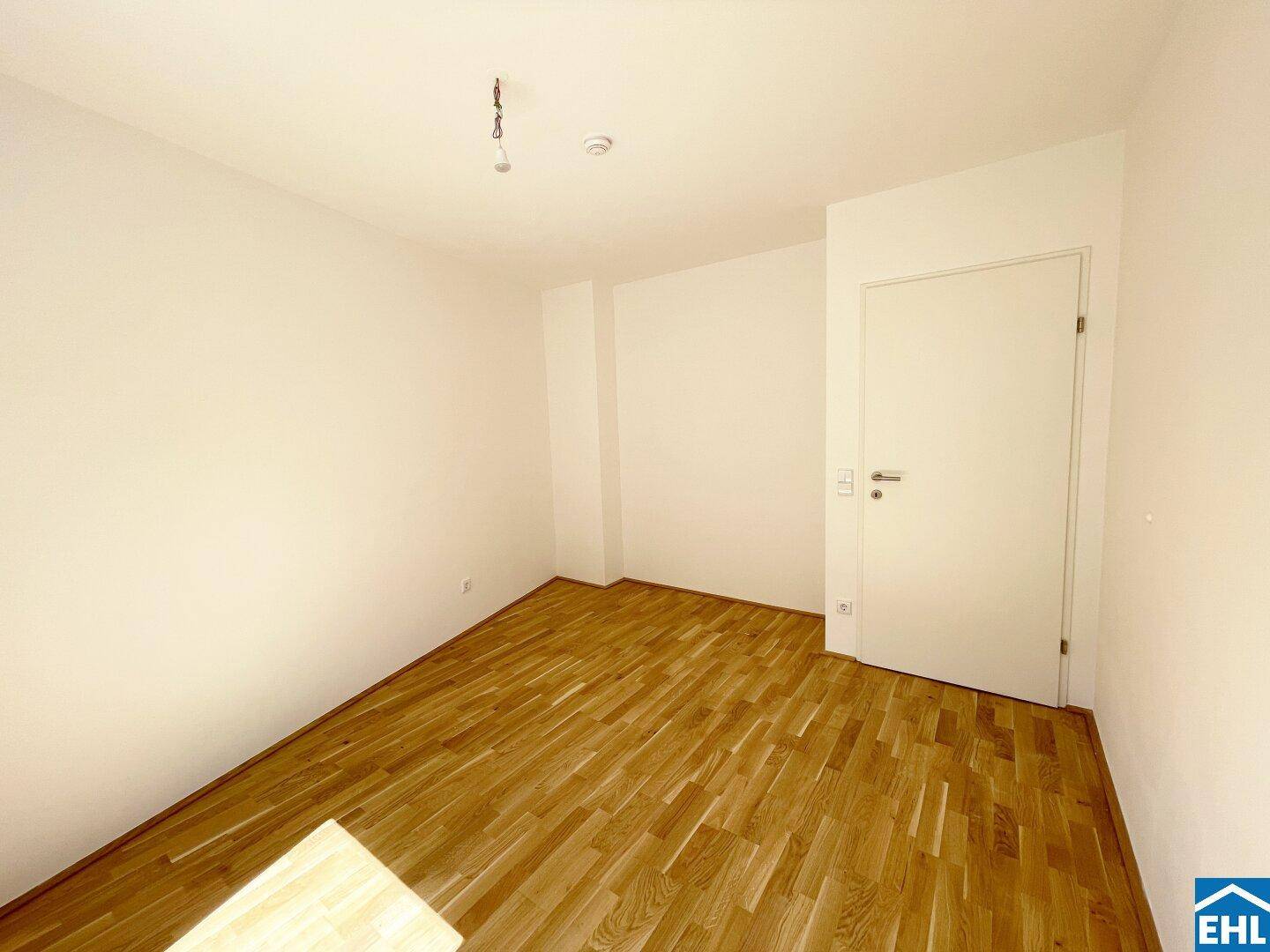 Unmöbliertes Schlafzimmer mit hellem Parkettboden und einer modernen weißen Tür, ideal für Ruhe.