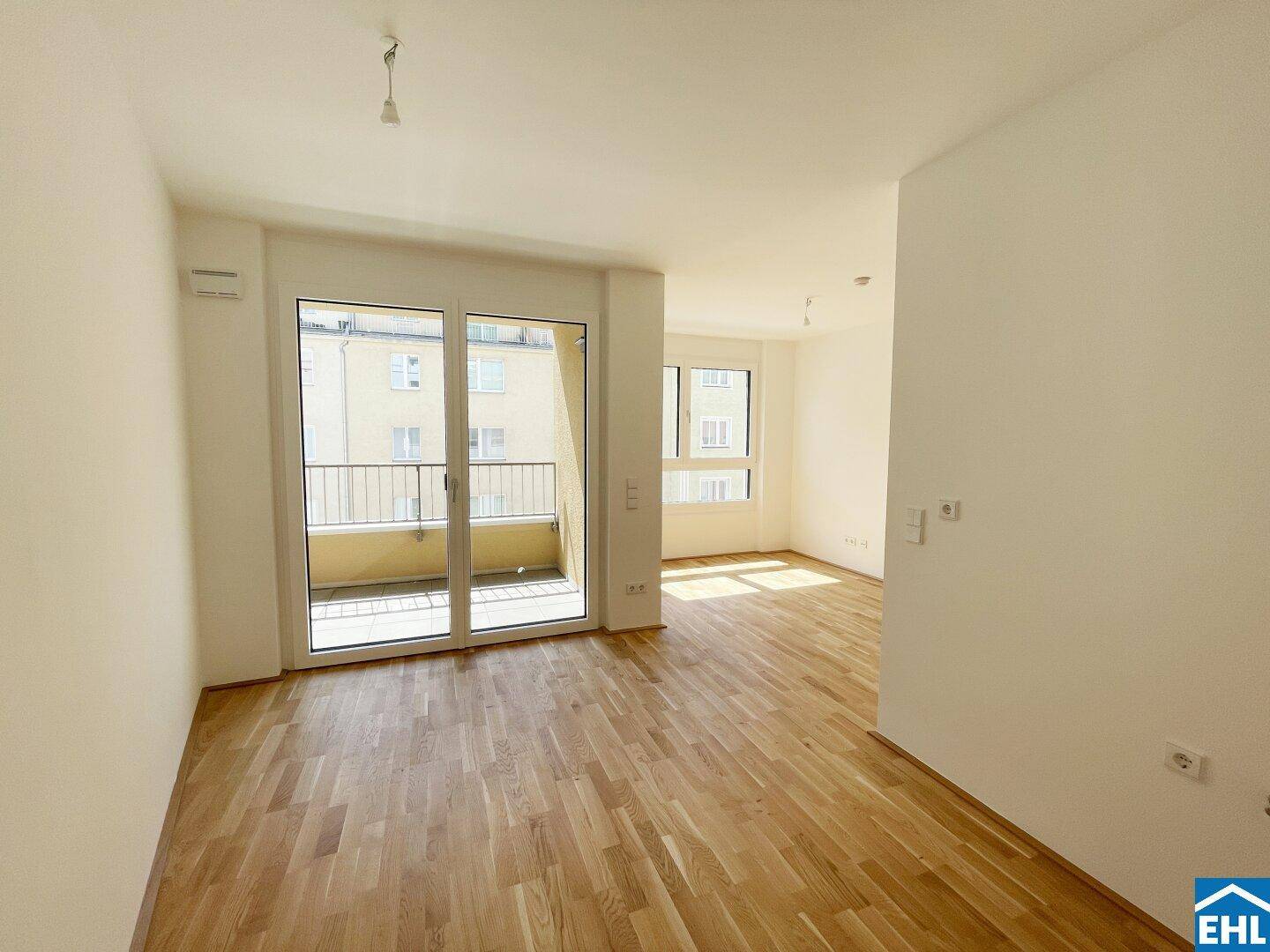 Geräumiges, helles Zimmer mit Holzboden und großem Balkonzugang, bietet viel Tageslicht.