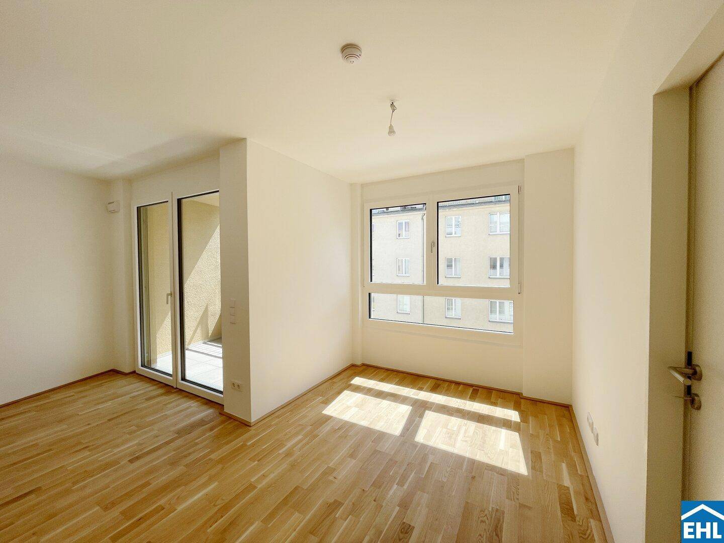 Helles Zimmer mit Parkettboden und Zugang zu einem Balkon, ideal als Wohn- oder Schlafbereich.