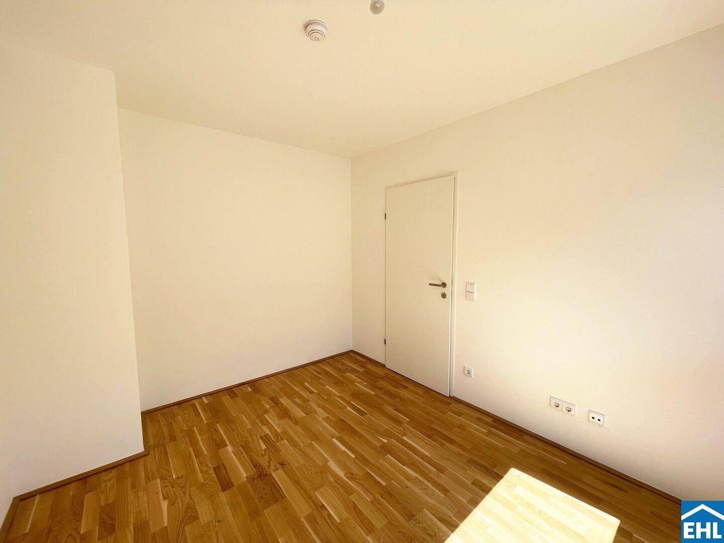 Helles Zimmer mit Parkettboden und weißer Tür, bietet vielseitige Nutzungsmöglichkeiten.