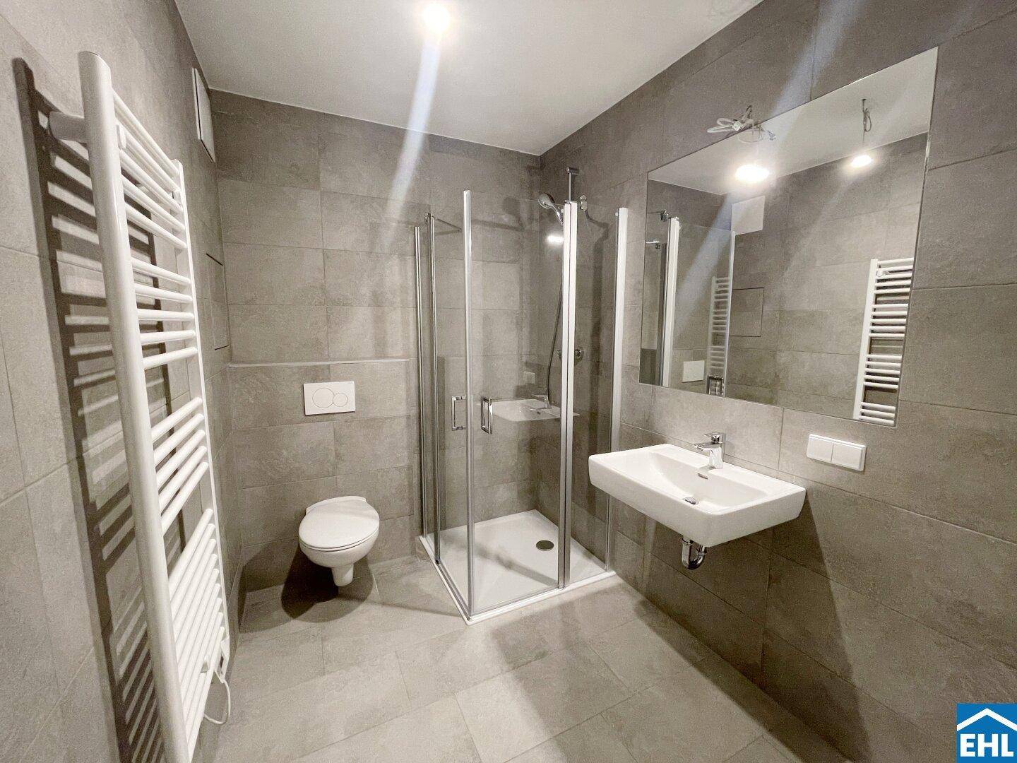 Modernes Badezimmer mit grauen Fliesen, Dusche, WC und beheiztem Handtuchhalter.