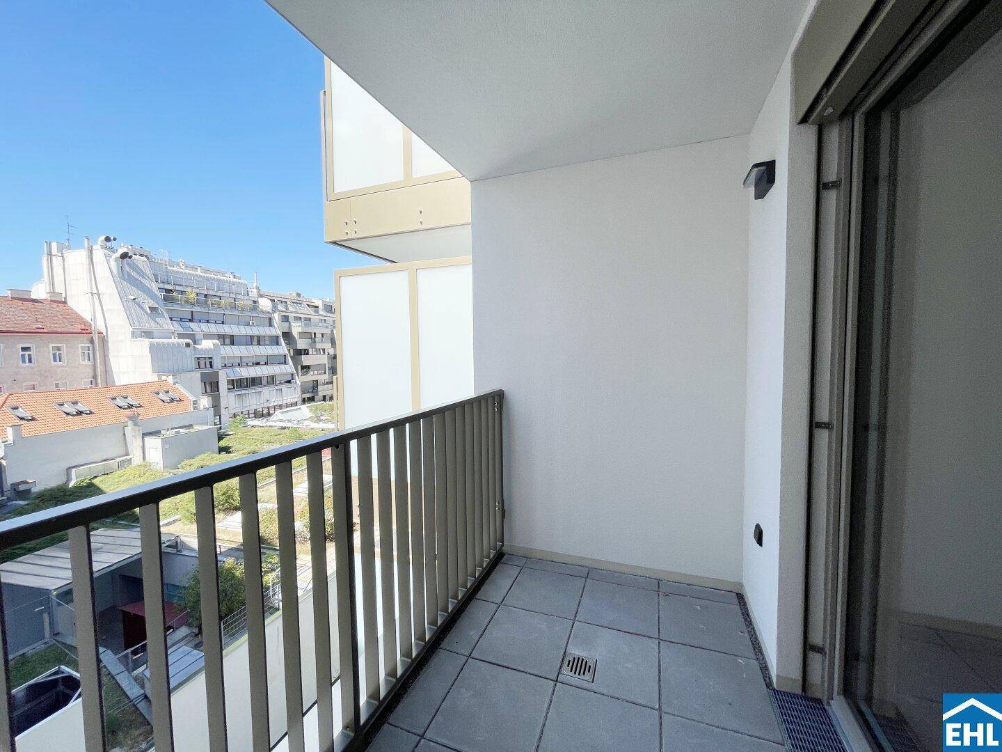 Heller Balkon mit Fliesenboden und Blick auf die umliegenden Gebäude unter blauem Himmel.