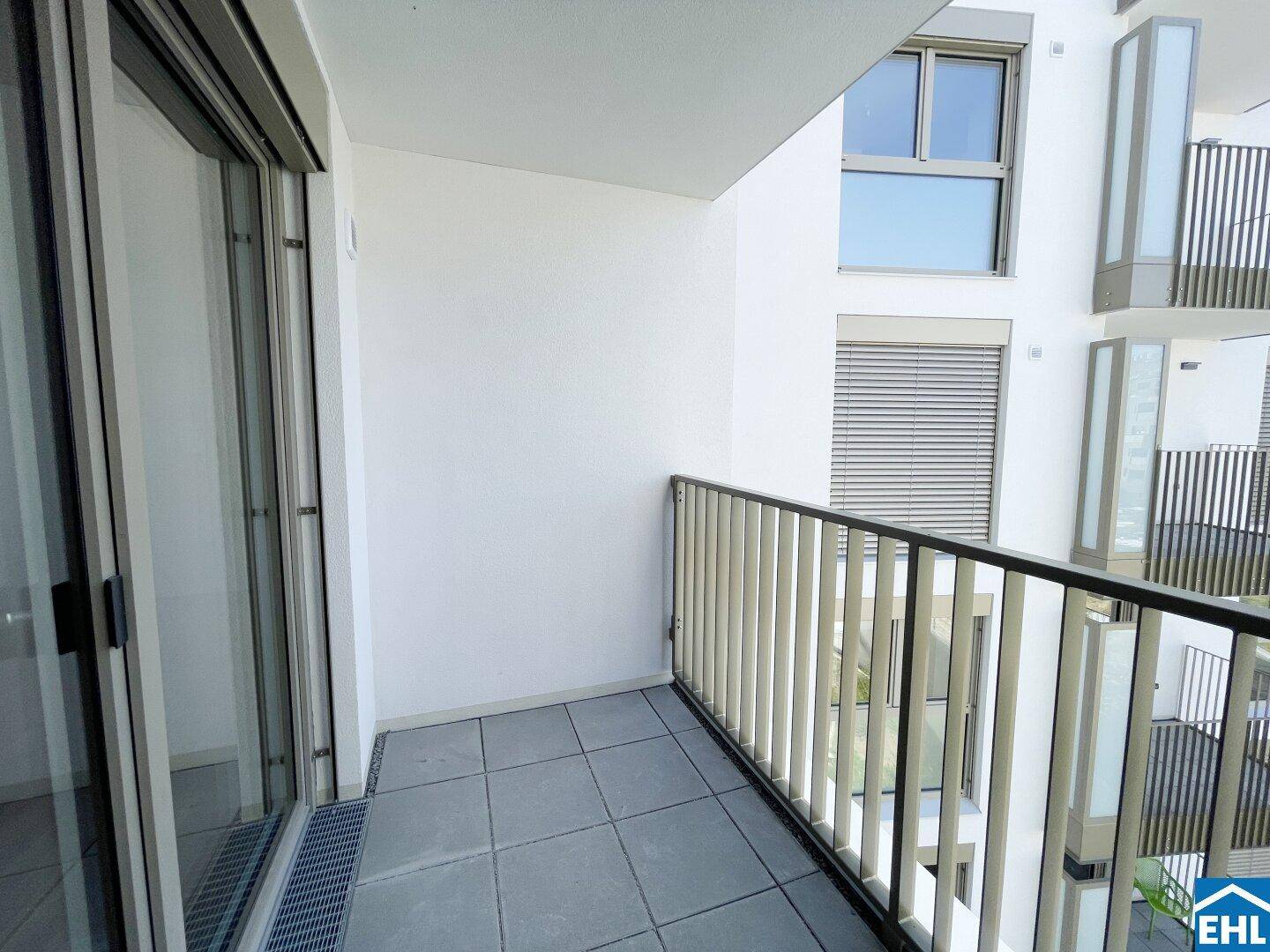 Moderner Balkon mit Fliesenboden und Blick auf die benachbarten Gebäude.