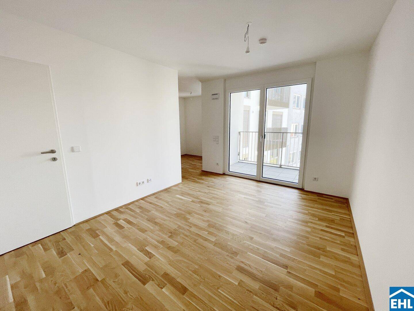 Geräumiger, heller Wohnbereich mit Parkettboden und Zugang zu einem Balkon.