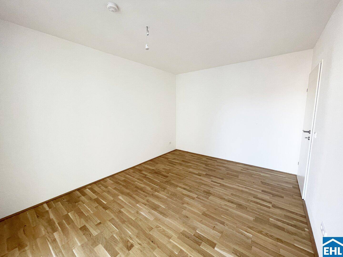 Helles Schlafzimmer mit Parkettboden und weißen Wänden, bereit zur individuellen Gestaltung.