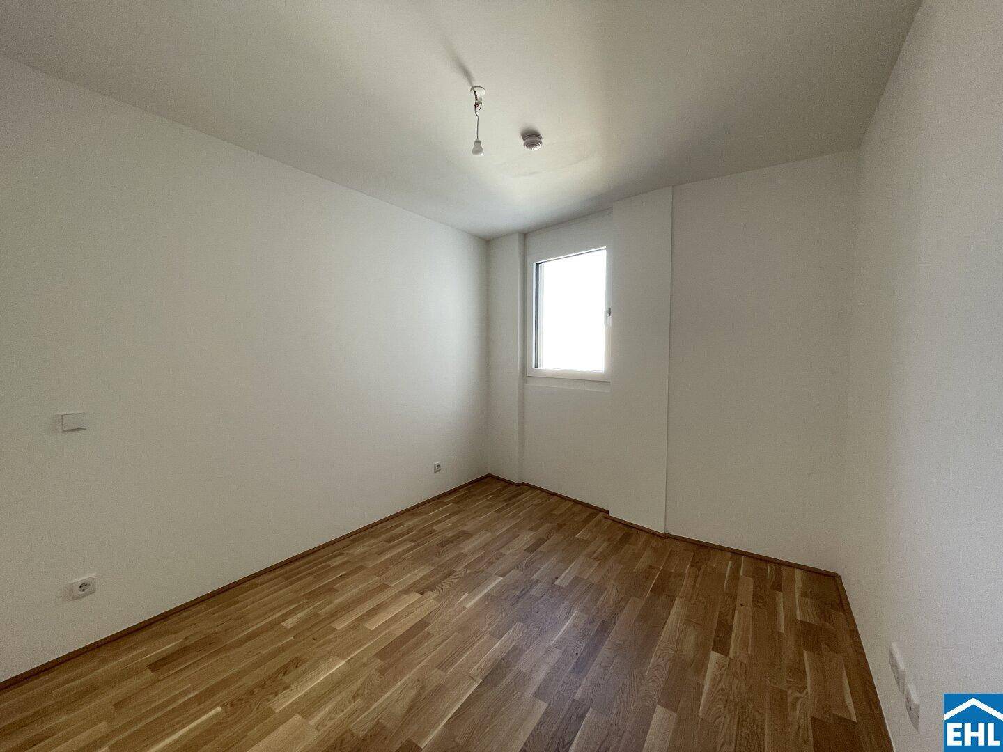 Helles Schlafzimmer mit Parkettboden und Fenster, ideal für Ruhe und Erholung.