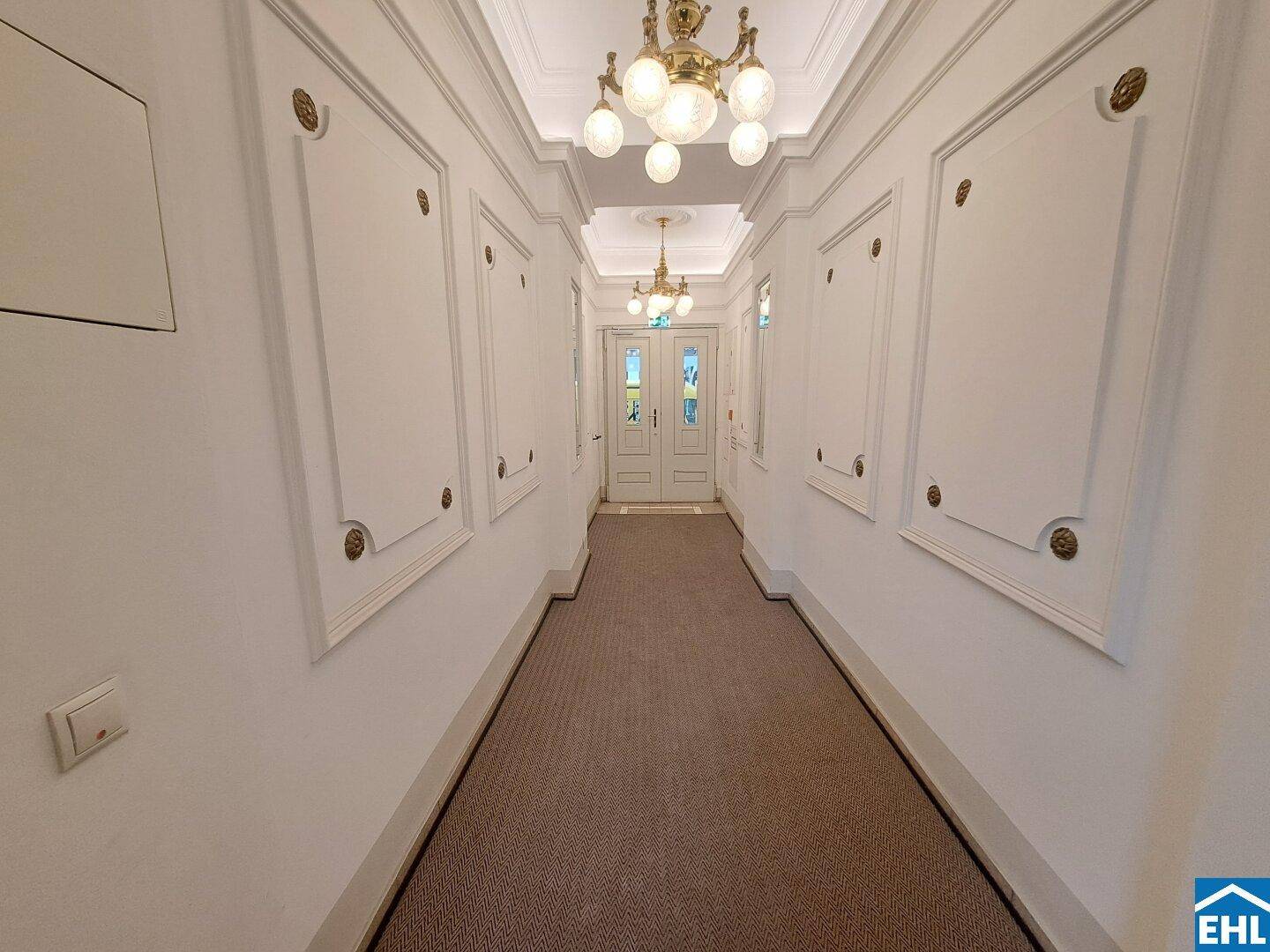 Langer, eleganter Flur mit Teppichboden, verzierten Wandpaneelen und klassischen Deckenleuchten.